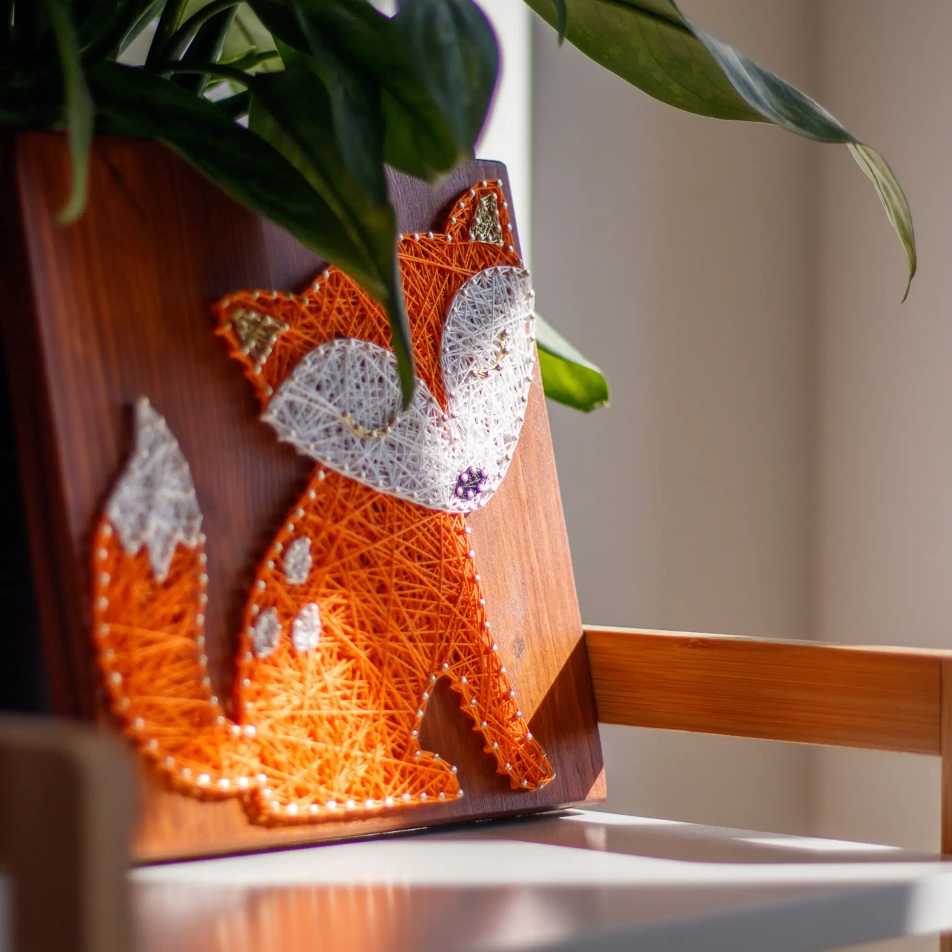 Side view of the completed fox string art pattern, showcasing intricate orange and white threadwork, beautifully lit by natural light.