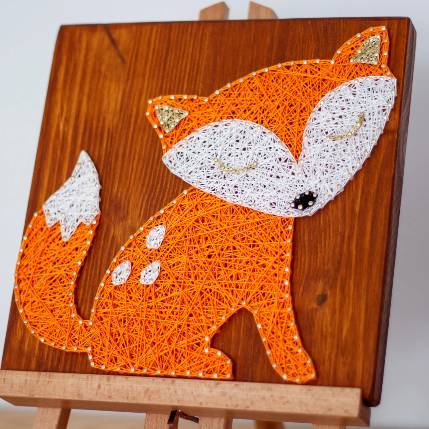 Front view of the fox string art pattern design, placed on an easel, featuring a sleeping orange fox with white details on a wooden background.