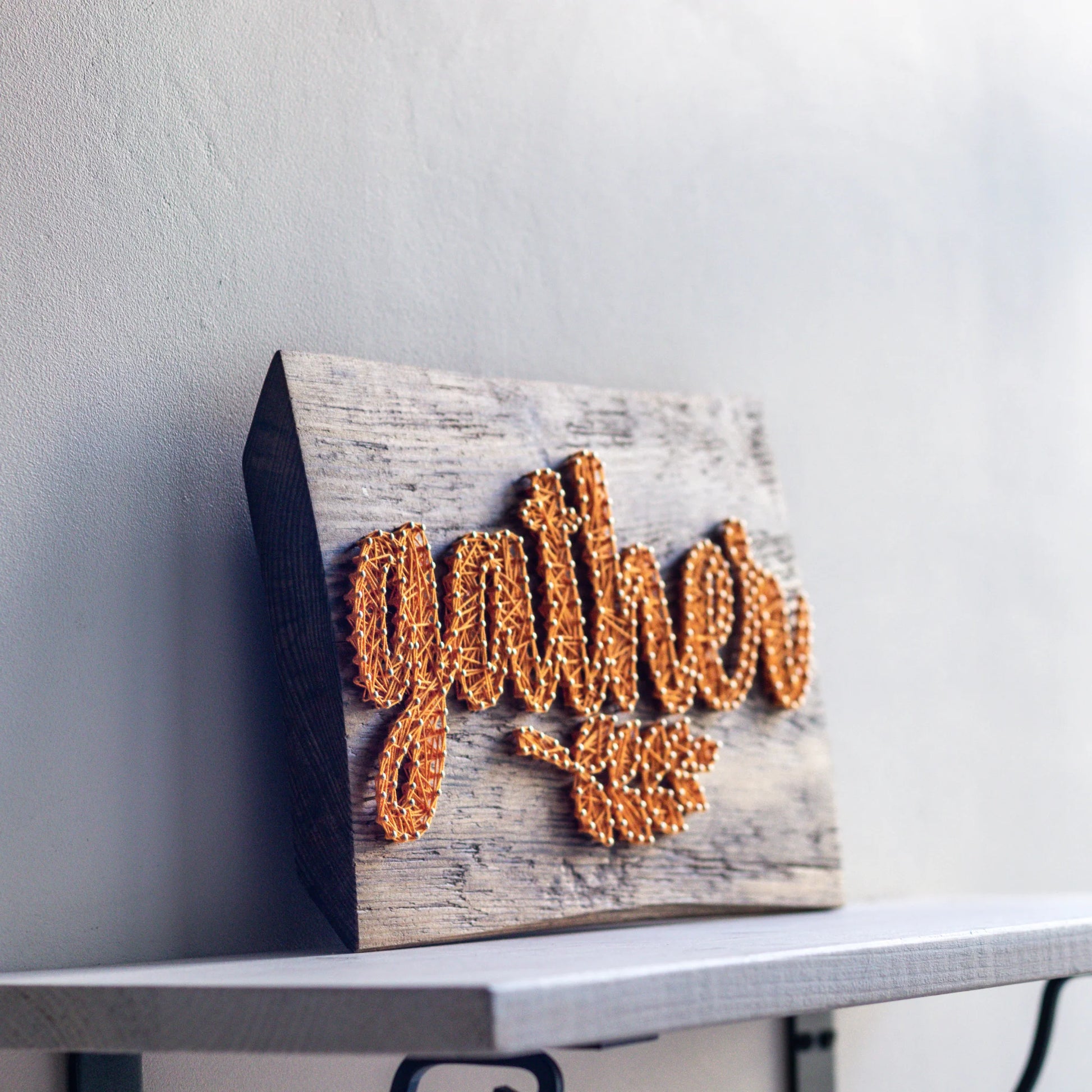 Angled view of the 'Gather' string art fall sign, displaying the raised letters made with yellow string. This digital pattern is designed for creating DIY rustic decor.