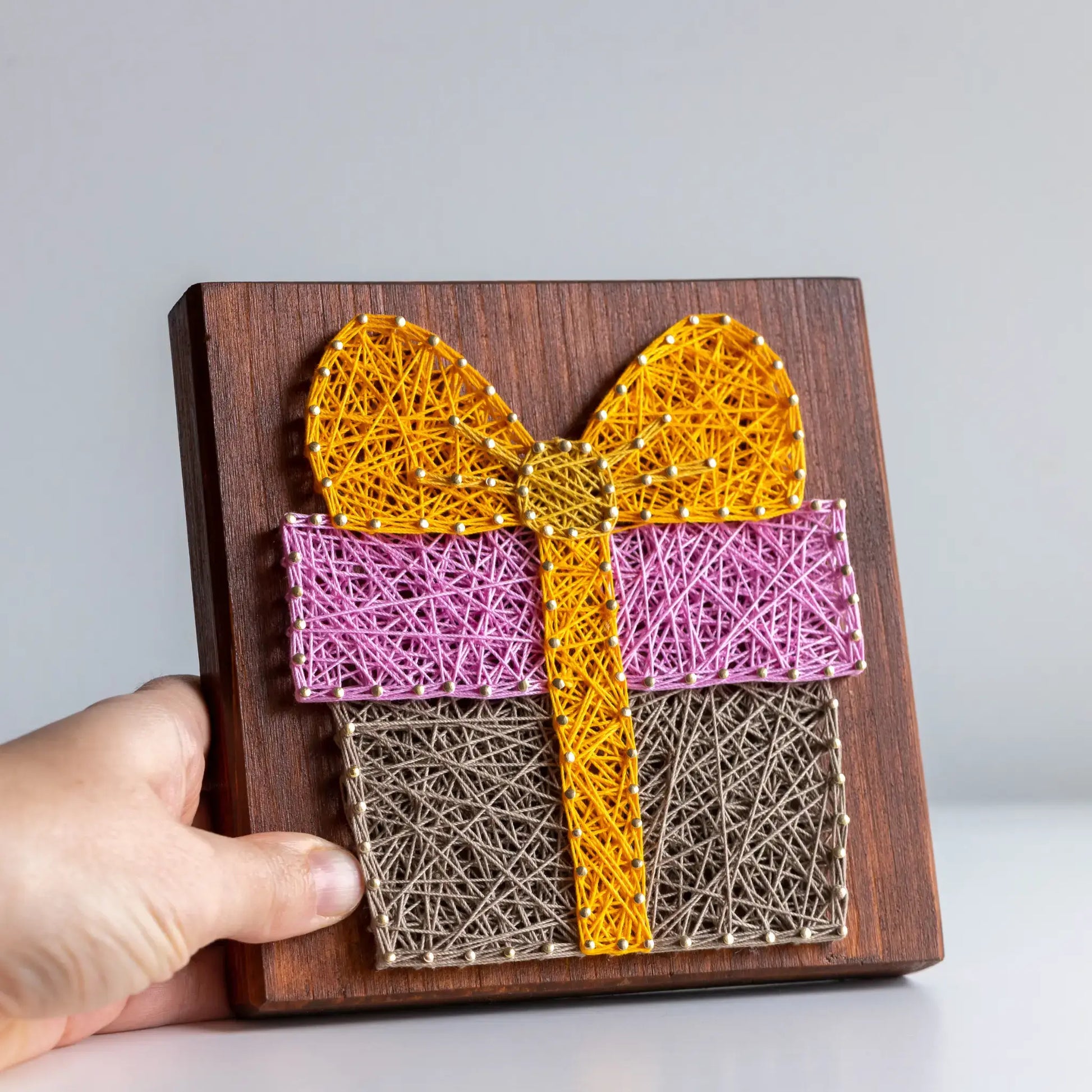 Close-up of colorful gift box string art pattern on wooden board, handmade DIY printable pattern.