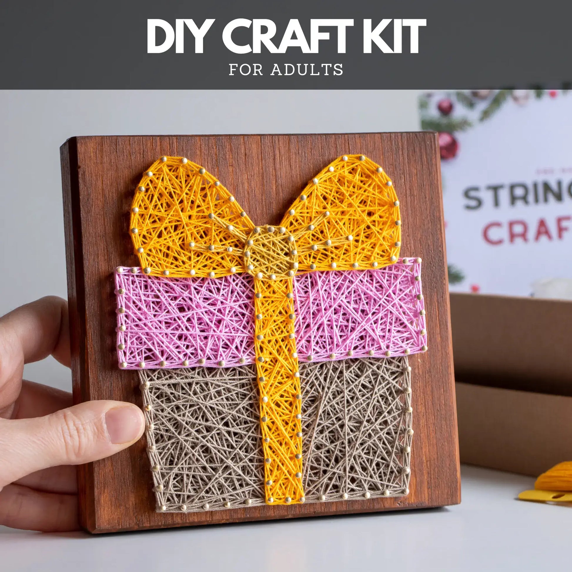 DIY craft kit for adults with string art of a gift box on a wooden board.