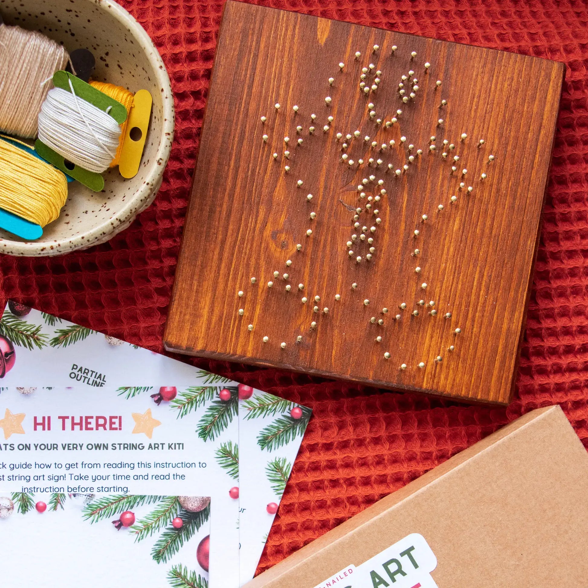 String art kit with wooden board, string, and instructions on a red surface