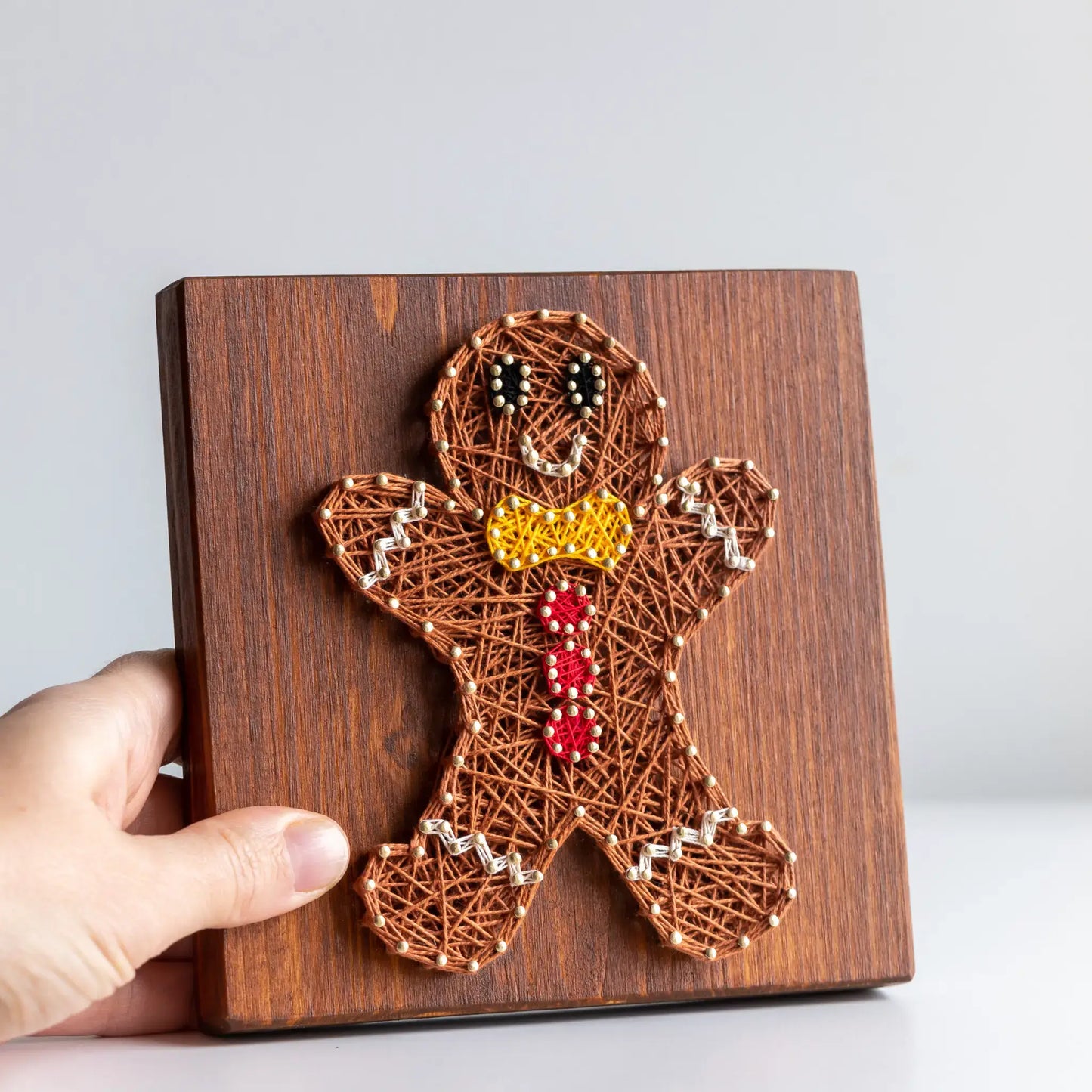 Wooden sign with string art gingerbread man design held by a hand on a light gray background