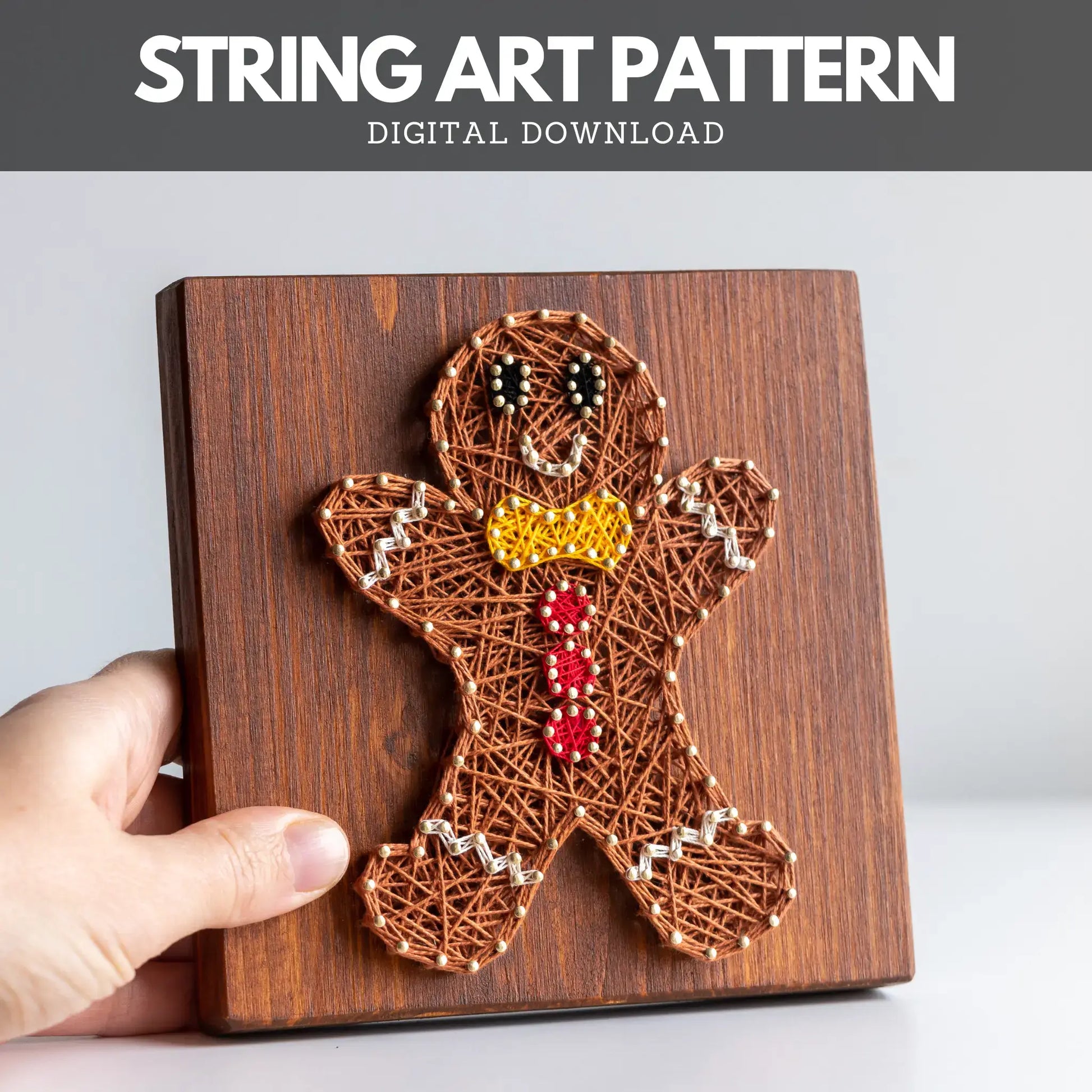 String art pattern of a gingerbread man on a wooden board with a hand holding it.