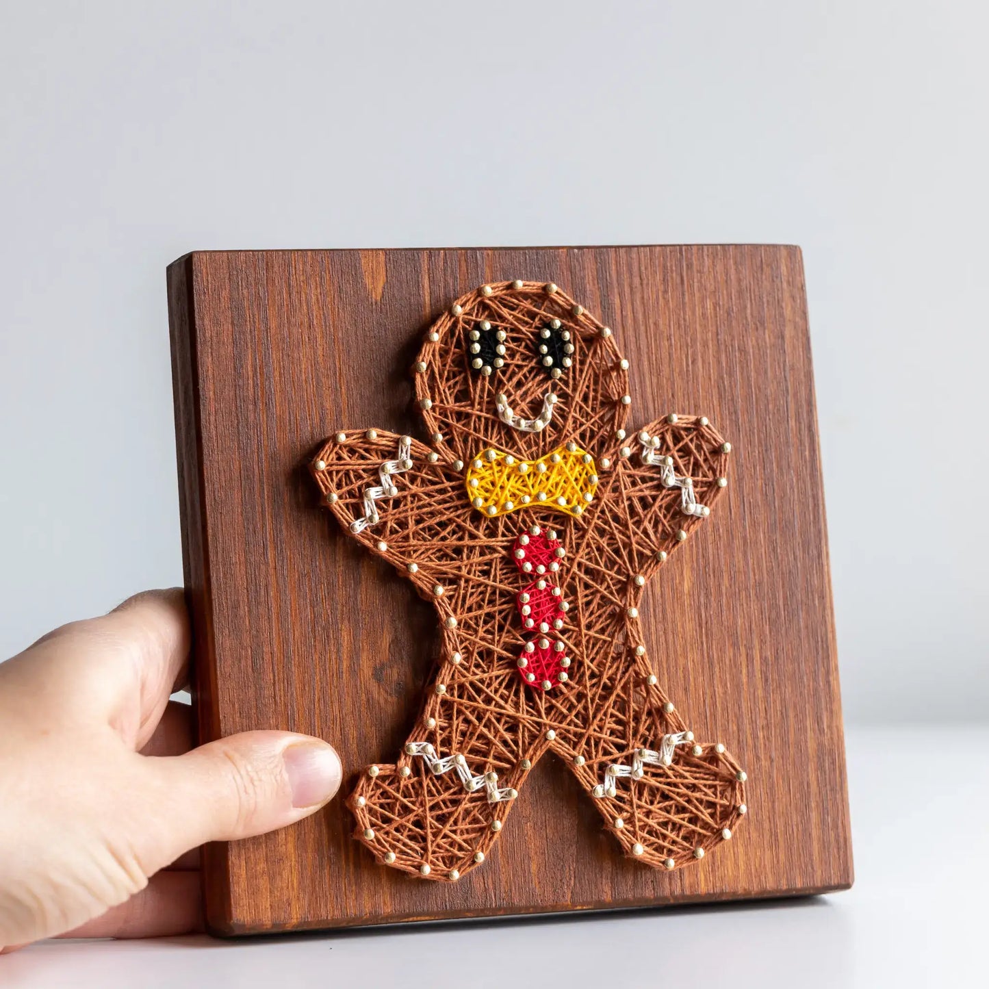 Close-up of gingerbread man string art pattern in brown, red, and yellow threads on wood base.