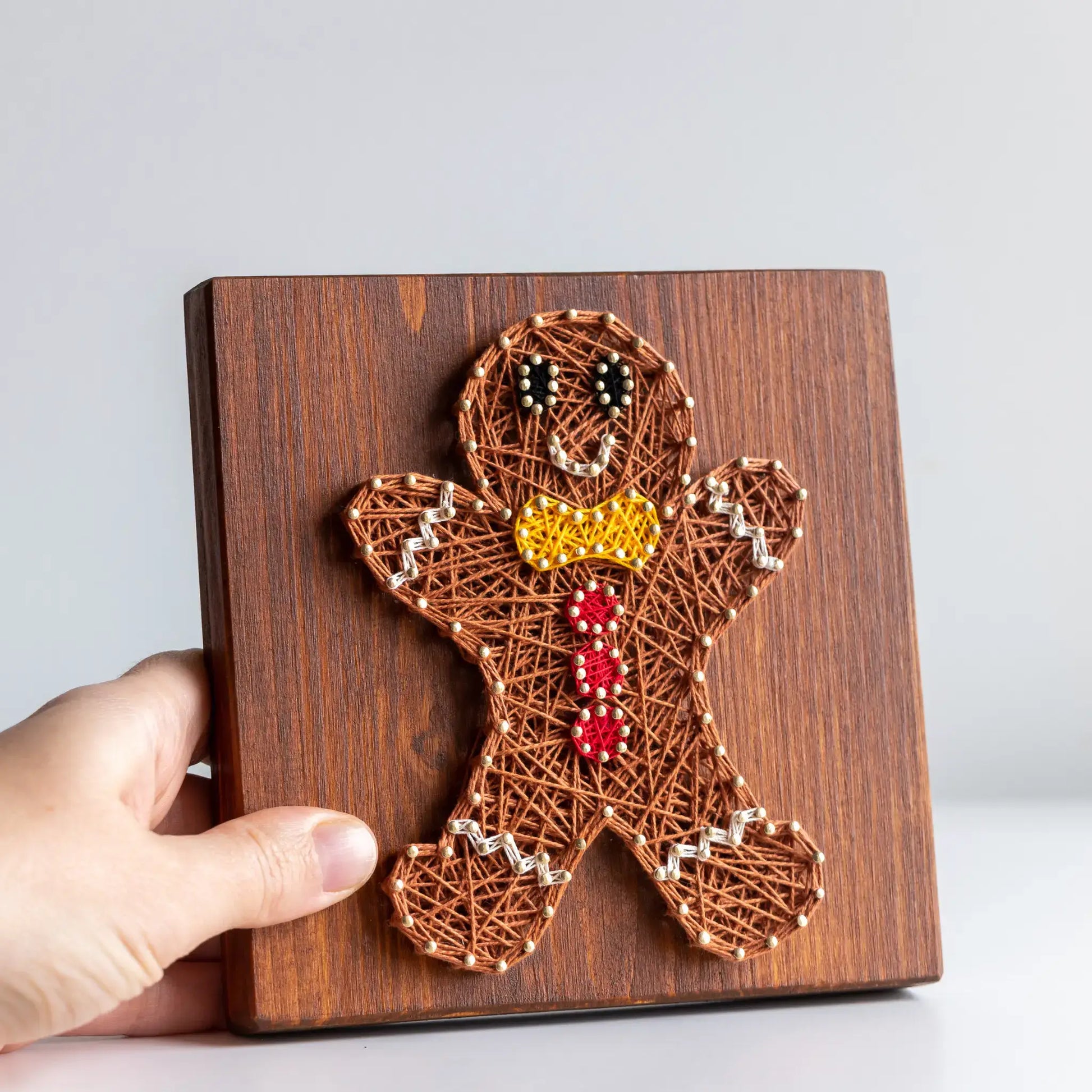 Close-up of gingerbread man string art pattern in brown, red, and yellow threads on wood base.
