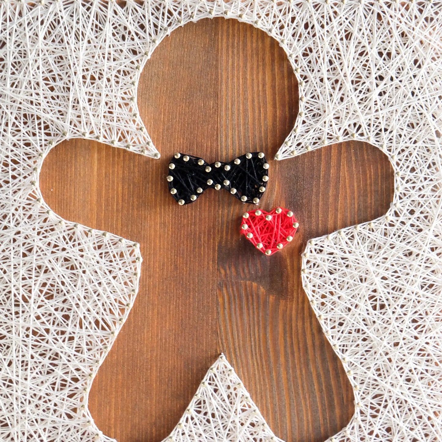 Close-up of a gingerbread string art pattern design with a wooden base, displaying intricate string work in white, black, and red threads.