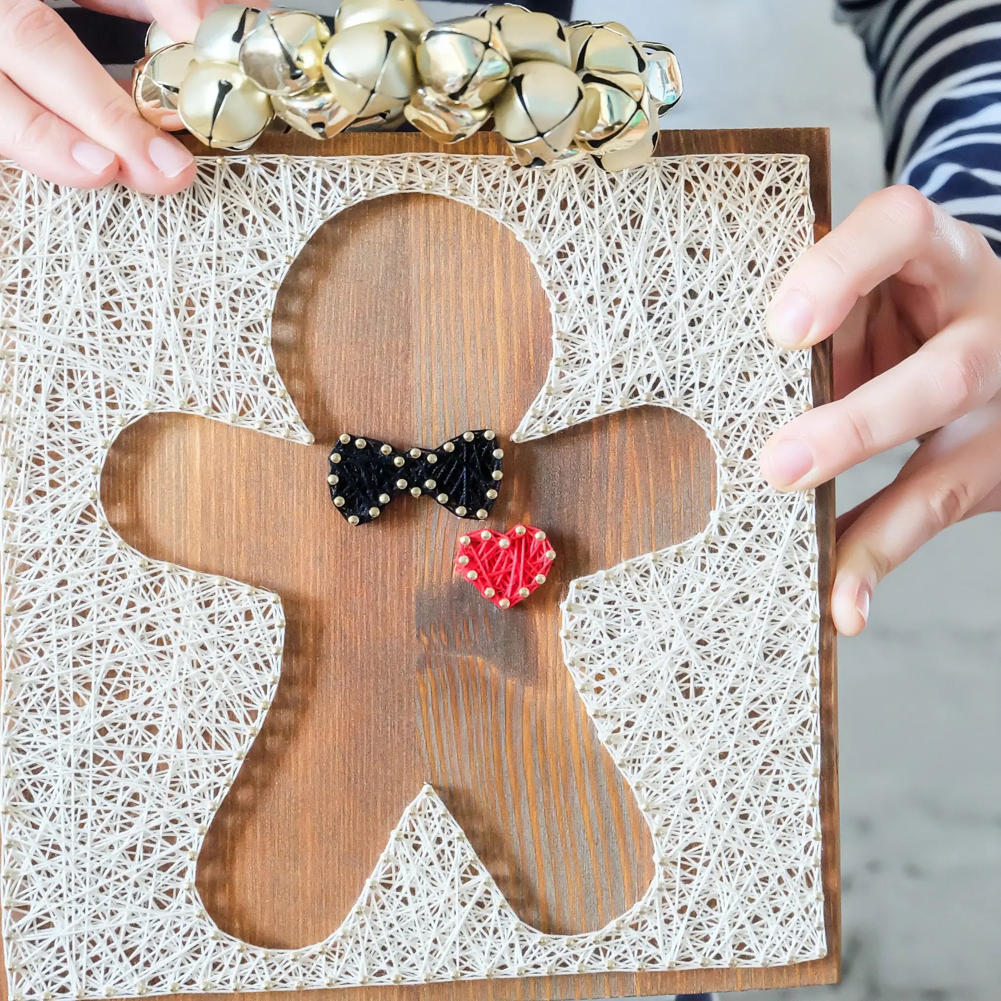 Gingerbread string art design held up against a festive background, featuring intricate string work with a bowtie and heart detail.