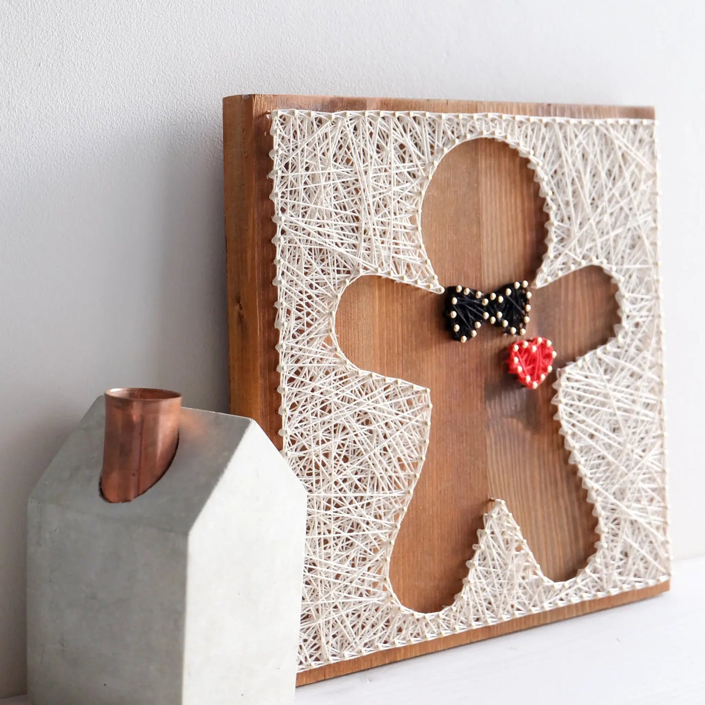 Side view of a gingerbread string art pattern design, featuring a black bowtie and a red heart, created with nails and threads.