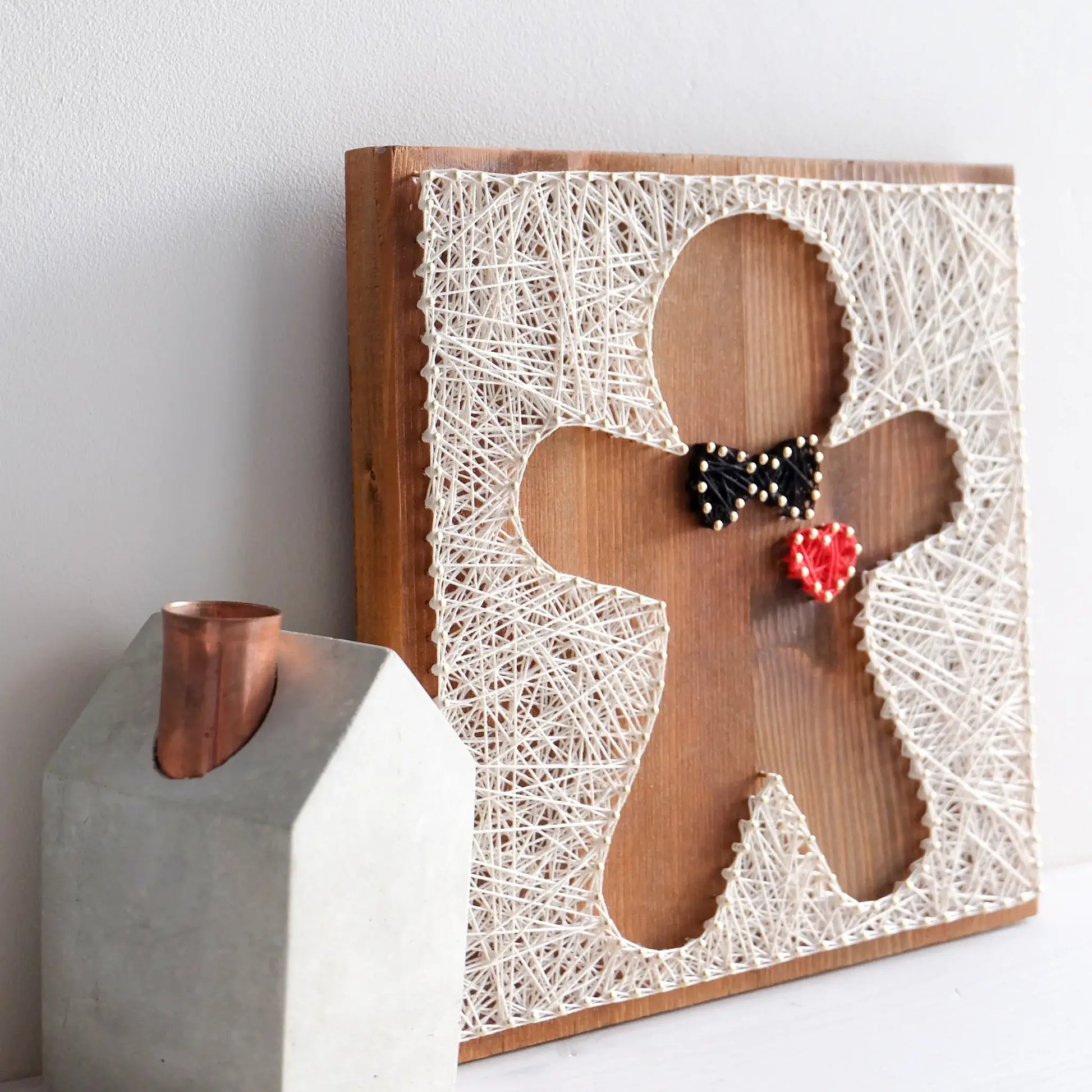 Side view of a gingerbread string art pattern design, featuring a black bowtie and a red heart, created with nails and threads.