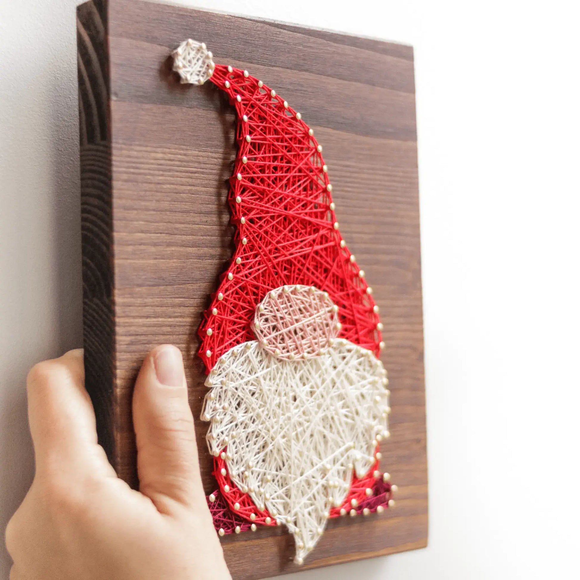 Side view of gnome string art highlighting detailed threading in red and white, carefully mounted on a wooden board.