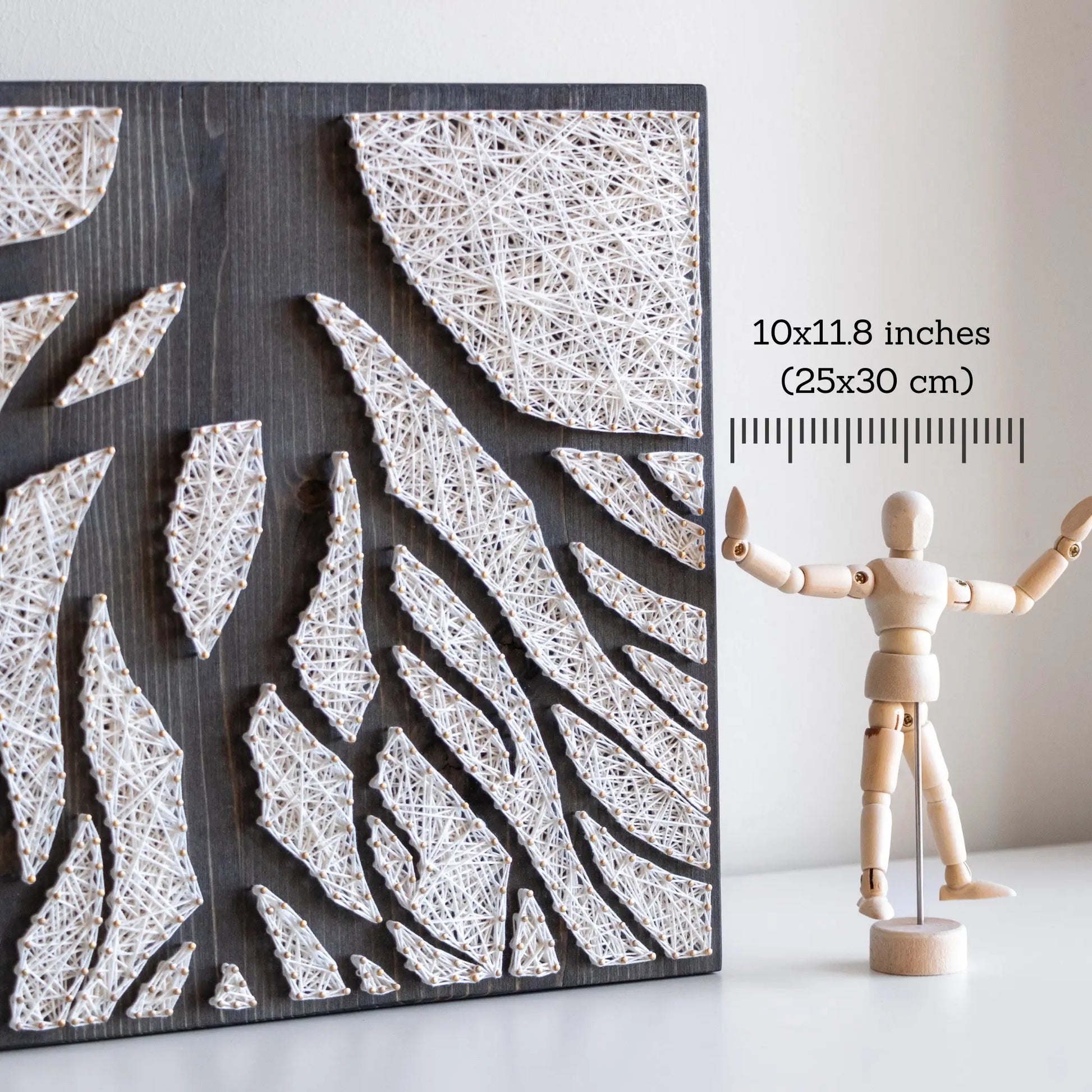 A piece of string art on a dark wooden board depicting abstract tree roots. The roots are created using white string and gold pins, arranged in various geometric shapes to form the intricate pattern of the tree roots.