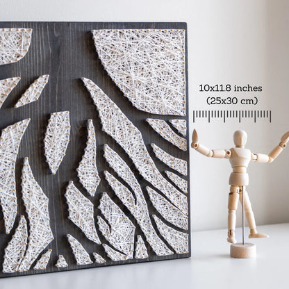 A piece of string art on a dark wooden board depicting abstract tree roots. The roots are created using white string and gold pins, arranged in various geometric shapes to form the intricate pattern of the tree roots.