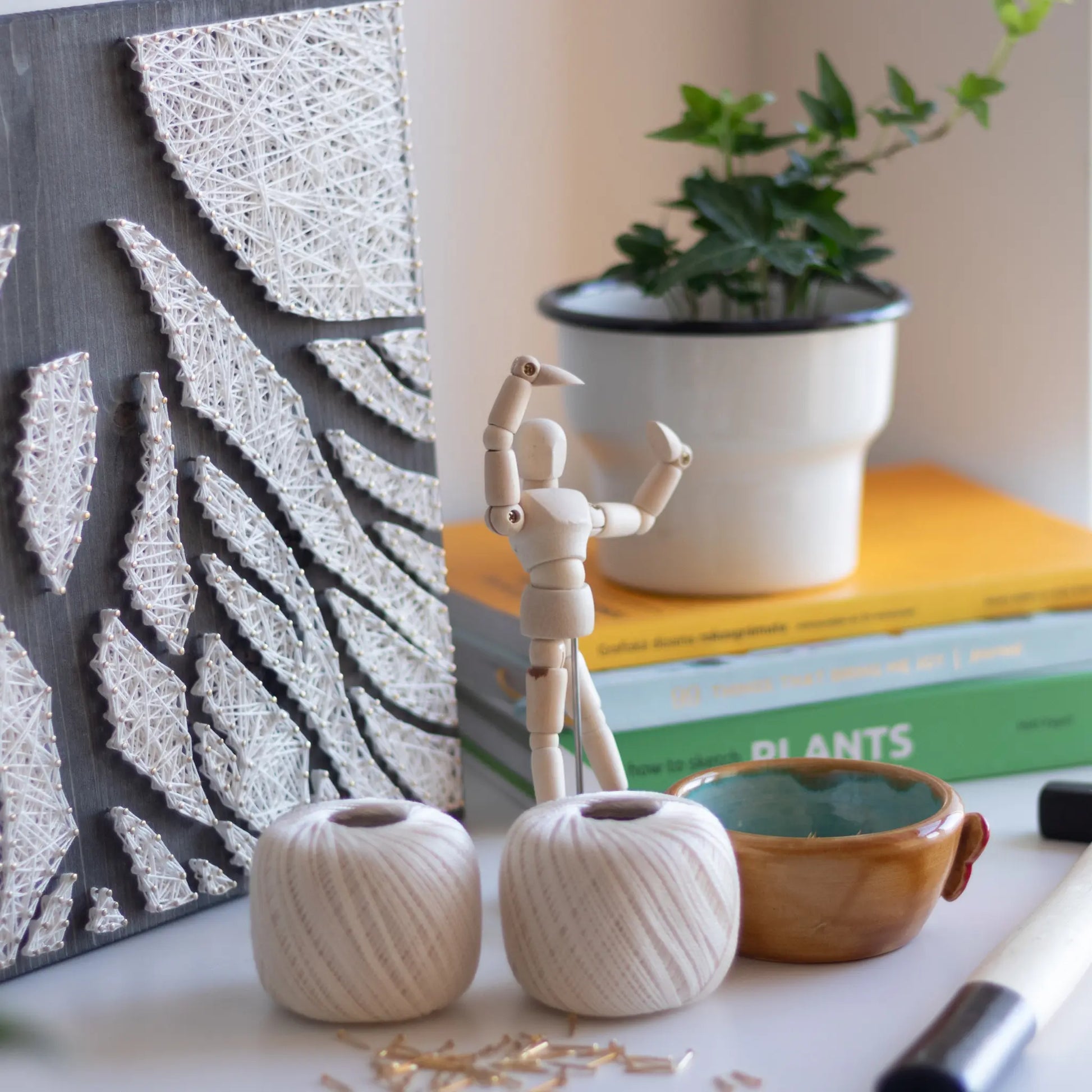 A piece of string art on a dark wooden board depicting abstract tree roots. The roots are created using white string and gold pins, arranged in various geometric shapes to form the intricate pattern of the tree roots.