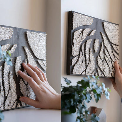 A piece of string art on a dark wooden board depicting abstract tree roots. The roots are created using white string and gold pins, arranged in various geometric shapes to form the intricate pattern of the tree roots.