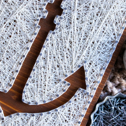 DIY string art kit featuring an anchor outlined with white thread on a rustic wooden board by GoodStrings - zoomed in