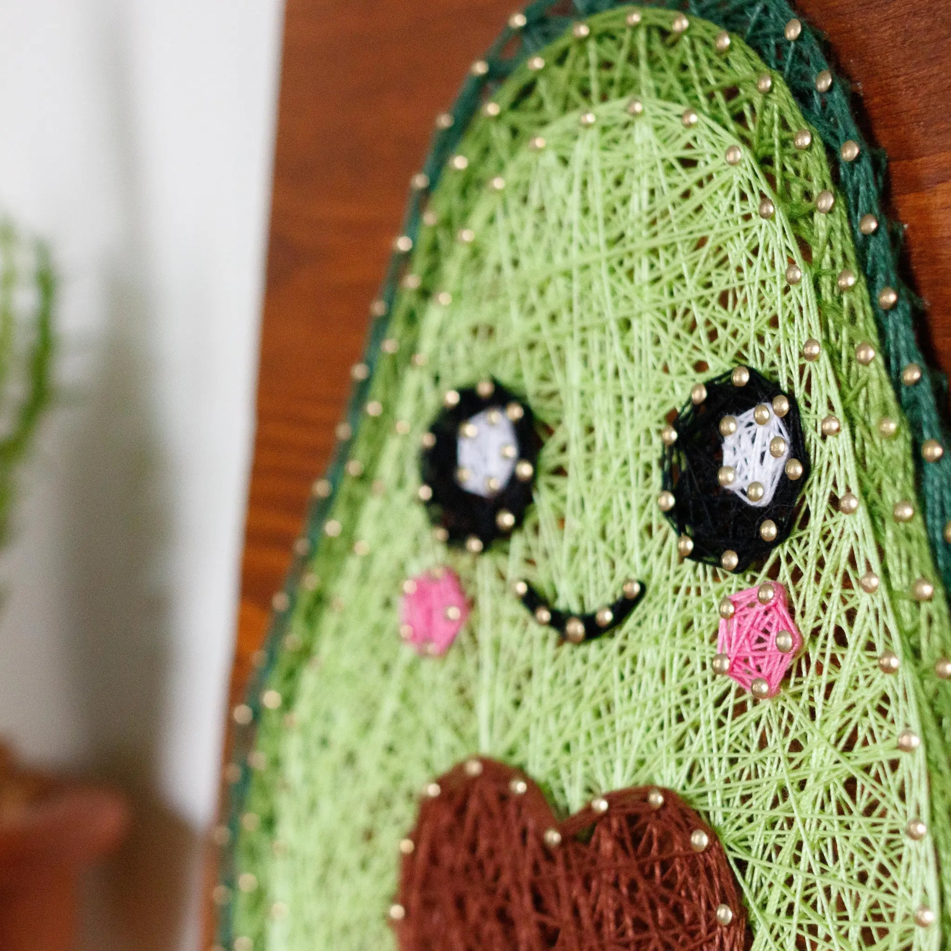 DIY string art kit featuring a cute avocado with a brown heart pit and smiling face created with threads on a wooden board by GoodStrings