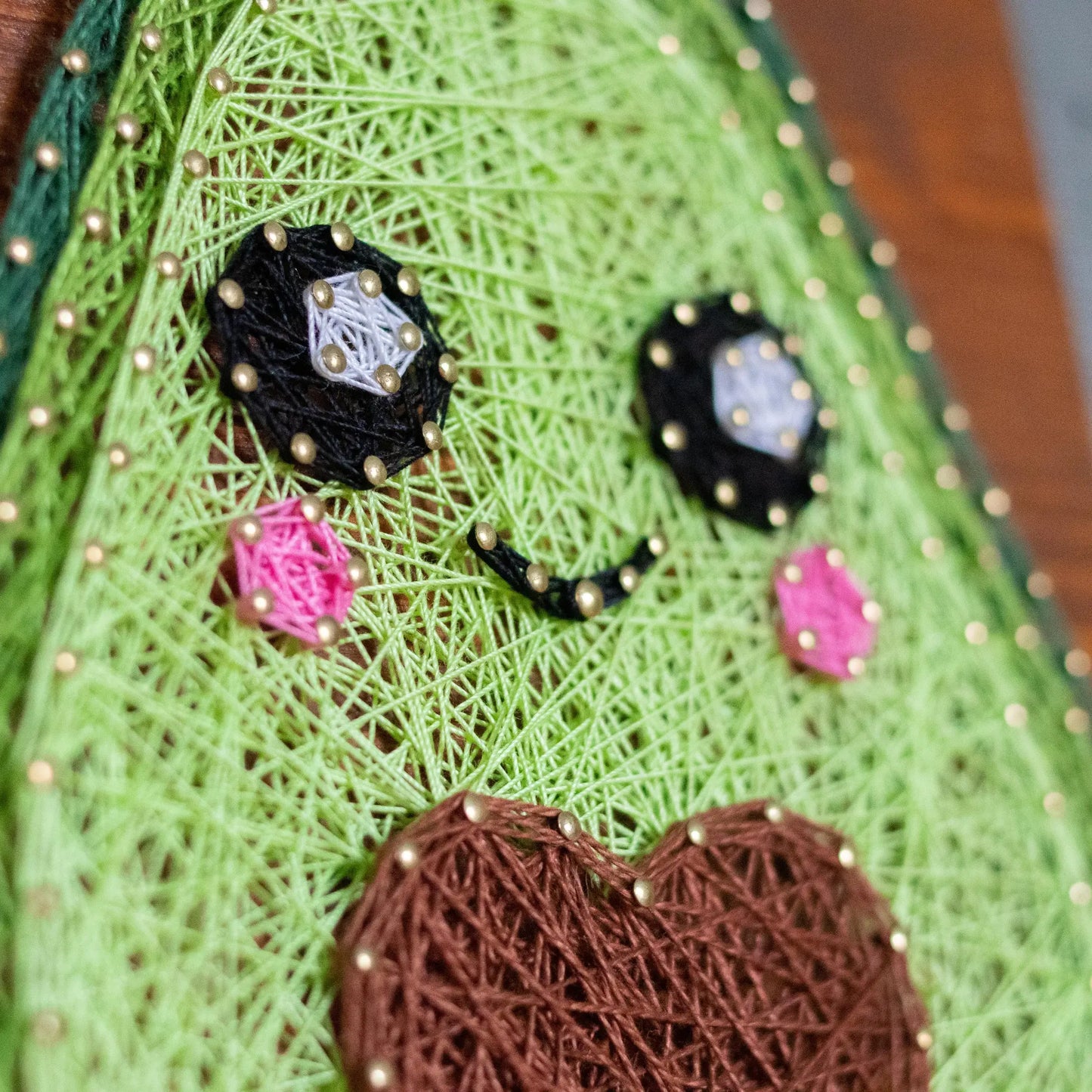 DIY string art kit featuring a cute avocado with a brown heart pit and smiling face created with threads on a wooden board by GoodStrings