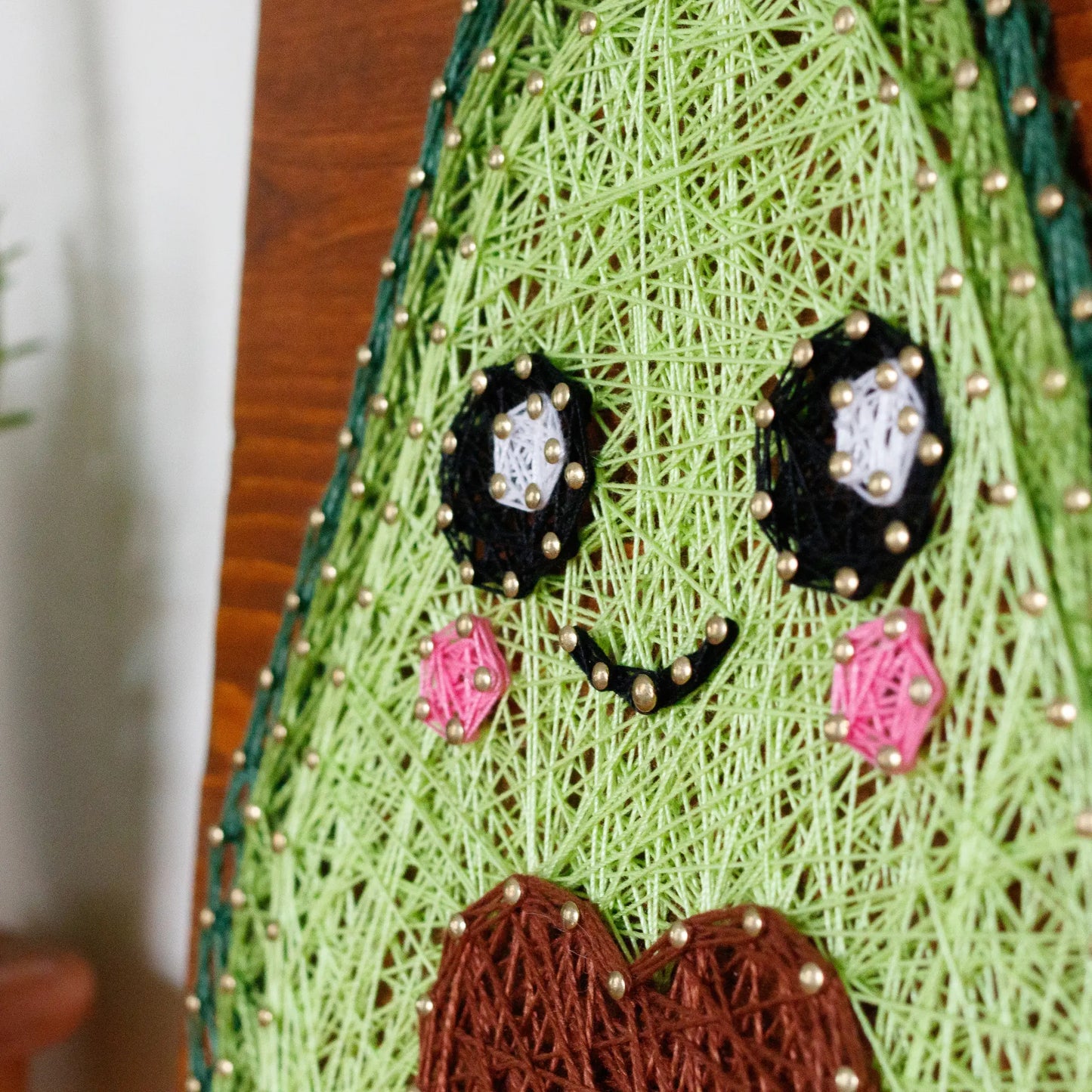 DIY string art kit featuring a cute avocado with a brown heart pit and smiling face created with threads on a wooden board by GoodStrings