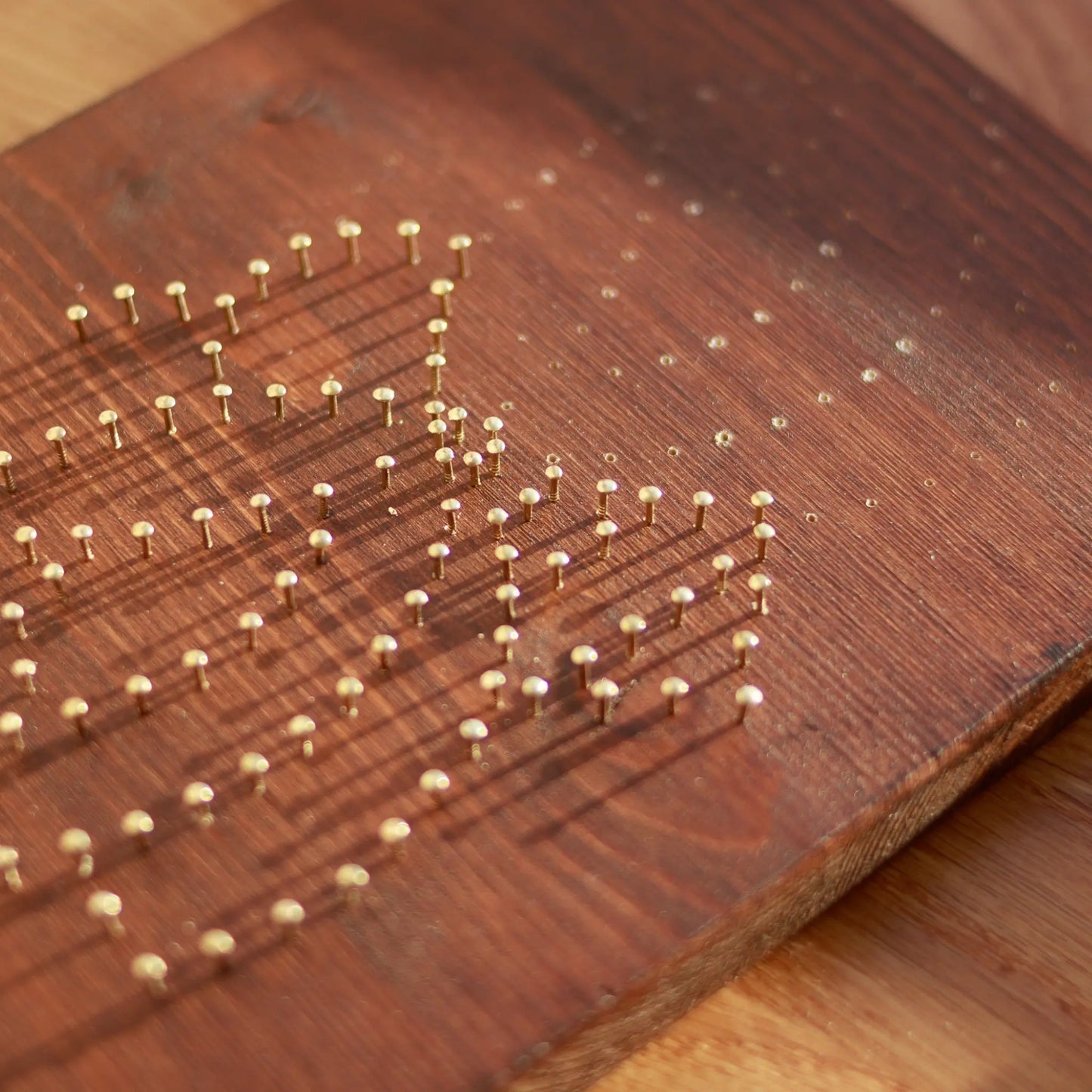 DIY string art kit featuring a bee outlined with black, yellow, and white thread on a rustic wooden board by GoodStrings - nails being hammered, in process