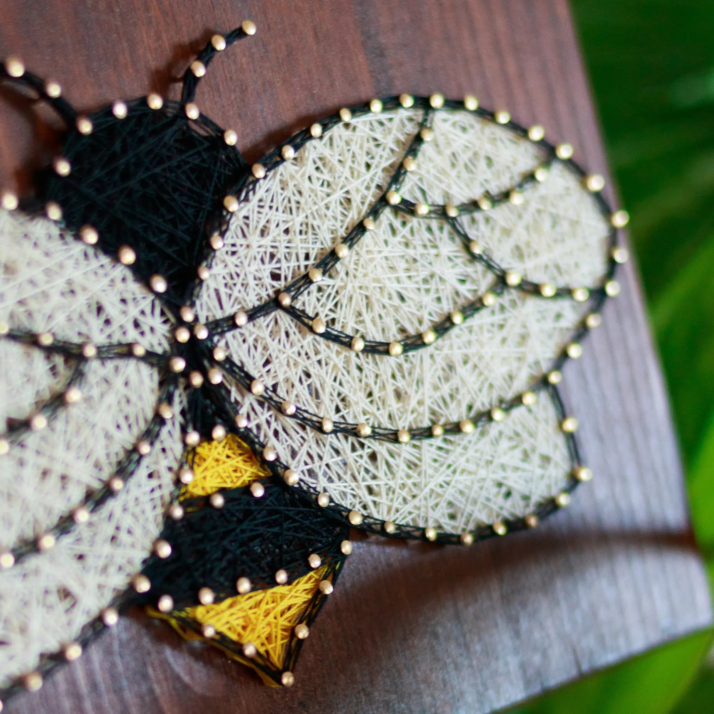 DIY string art kit featuring a bee outlined with black, yellow, and white thread on a rustic wooden board by GoodStrings - side view details