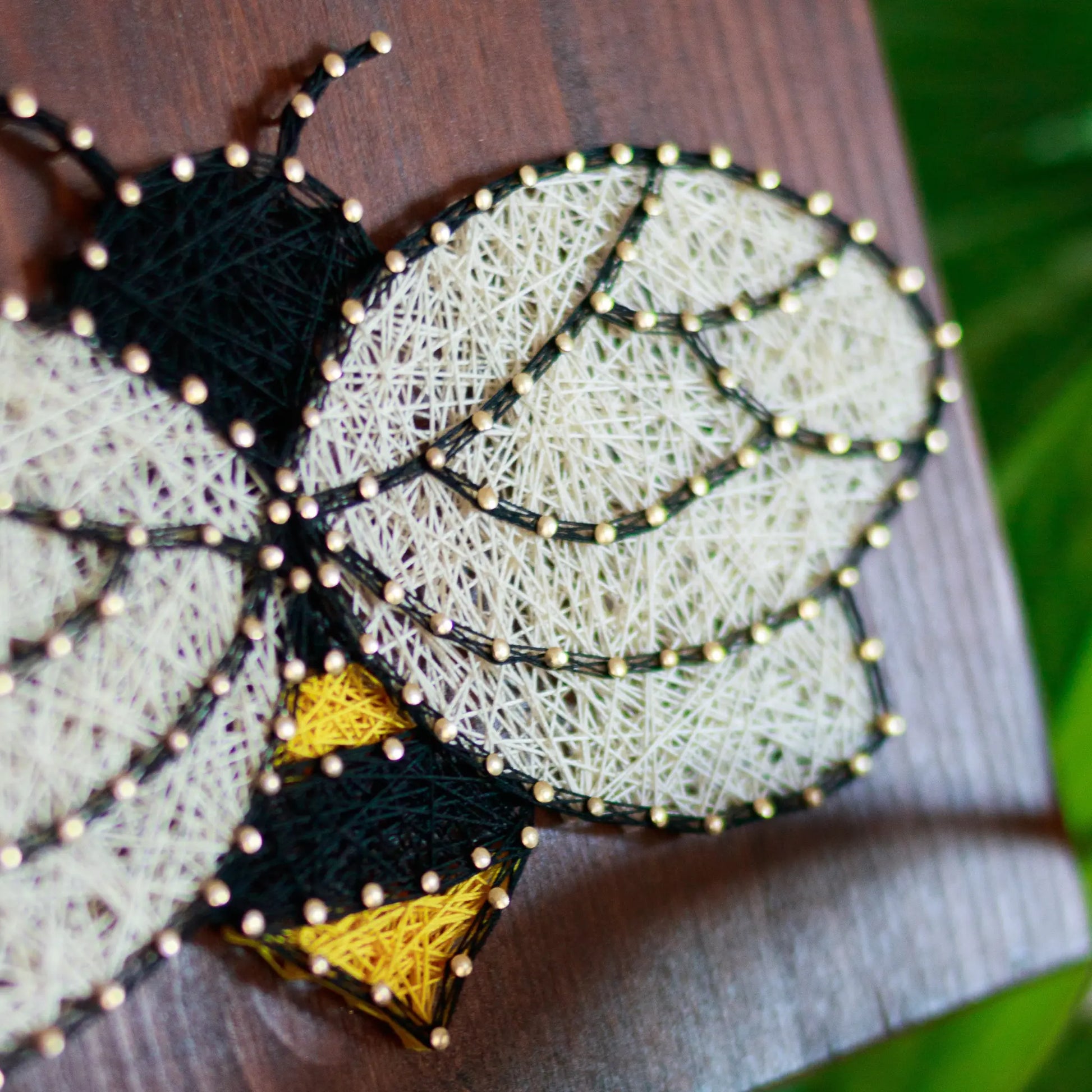 DIY string art kit featuring a bee outlined with black, yellow, and white thread on a rustic wooden board by GoodStrings - side view details