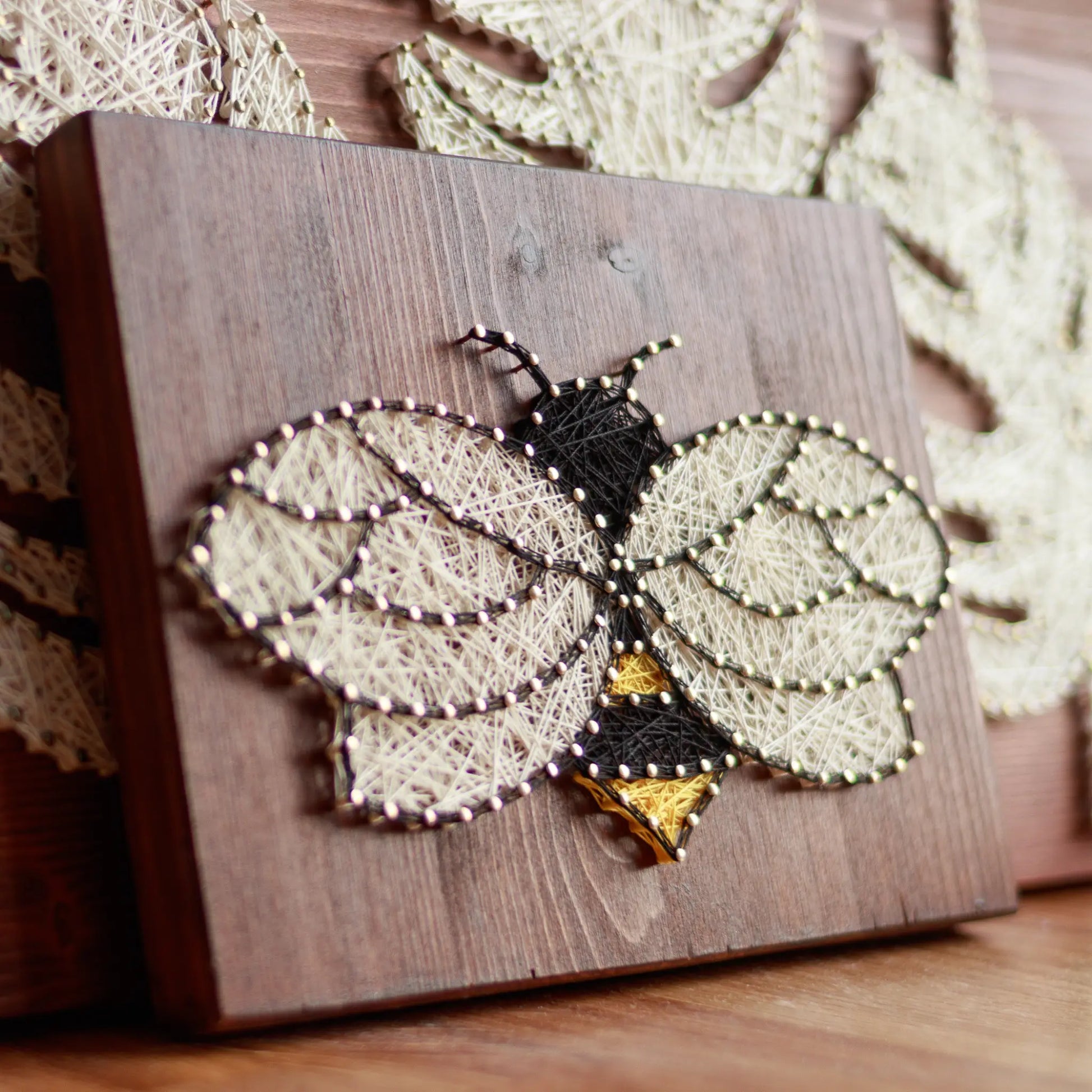 DIY string art kit featuring a bee outlined with black, yellow, and white thread on a rustic wooden board by GoodStrings - full side view