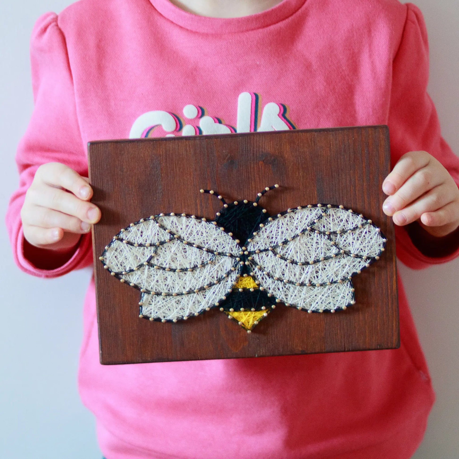 DIY string art kit featuring a bee outlined with black, yellow, and white thread on a rustic wooden board by GoodStrings - held in hands