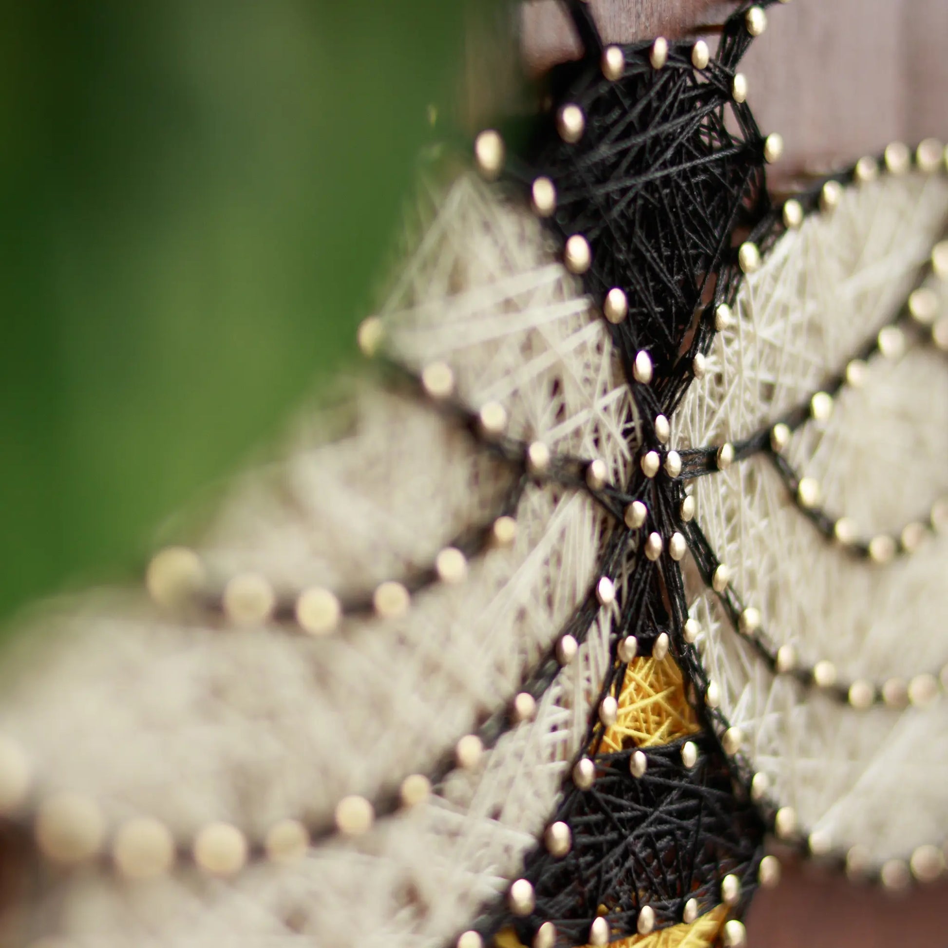 DIY string art kit featuring a bee outlined with black, yellow, and white thread on a rustic wooden board by GoodStrings - close-up details