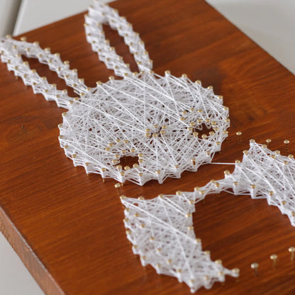 DIY string art kit featuring a cute bunny outlined with white, pink, and red thread on a rustic wooden board by GoodStrings - work in progress