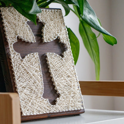 DIY string art kit featuring a cross silhouette with white threads on a dark wooden board by GoodStrings