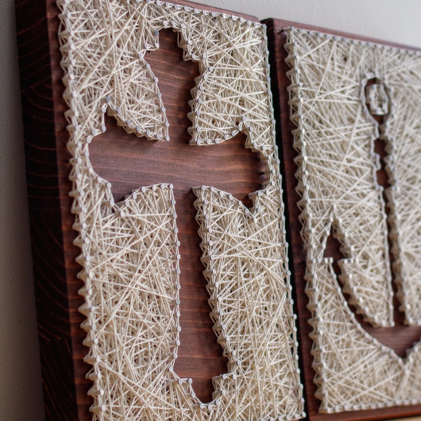 DIY string art kit featuring a cross silhouette with white threads on a dark wooden board by GoodStrings