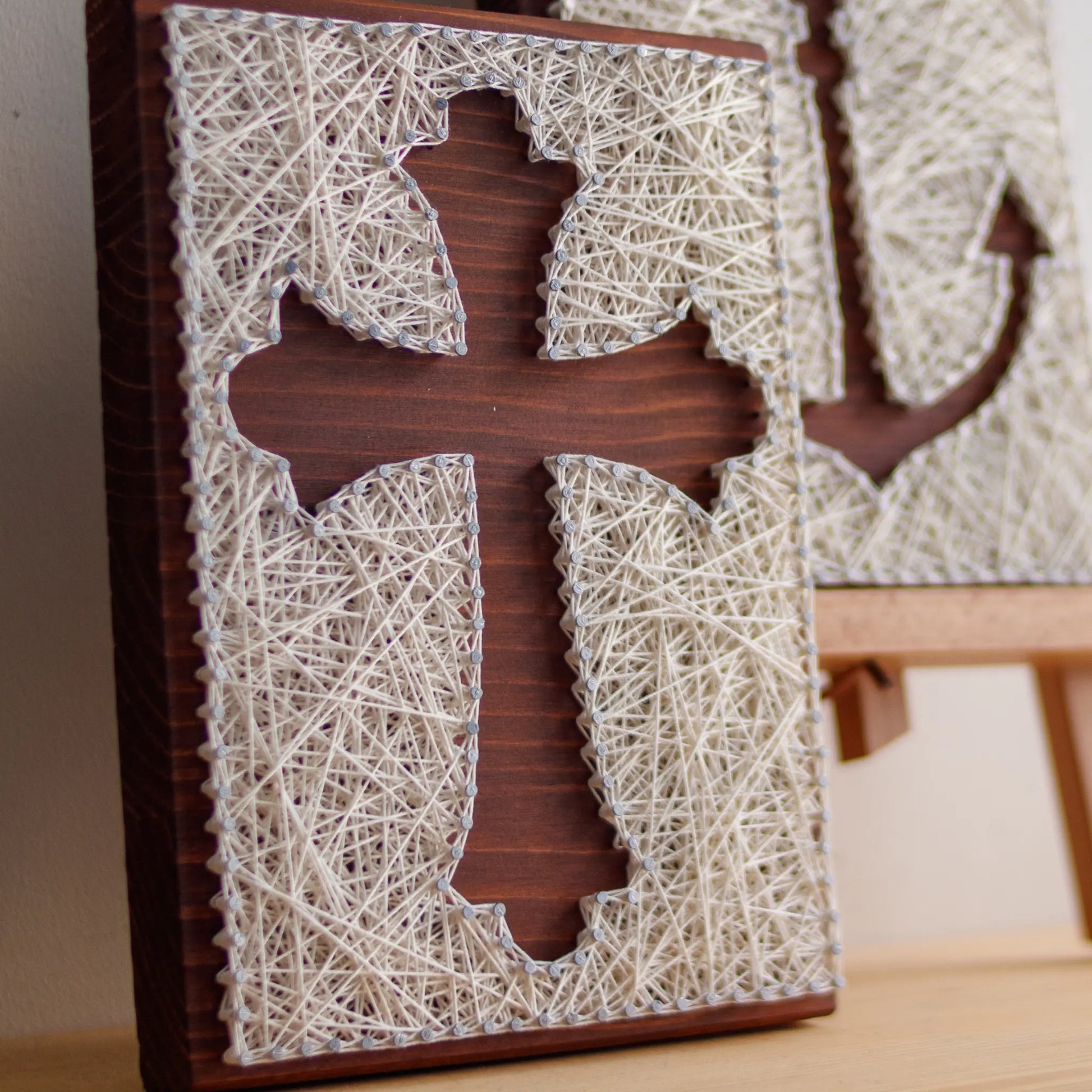 DIY string art kit featuring a cross silhouette with white threads on a dark wooden board by GoodStrings