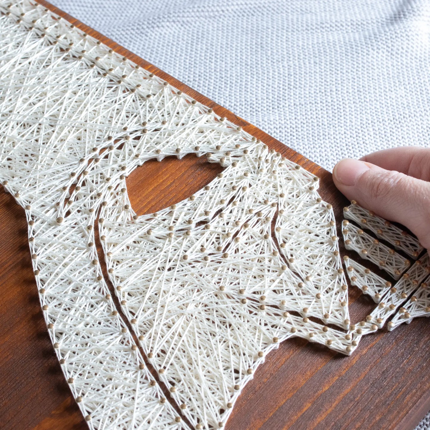 DIY string art kit featuring a silhouette of Darth Vader outlined with white thread on a rustic wooden board by GoodStrings - hand holding