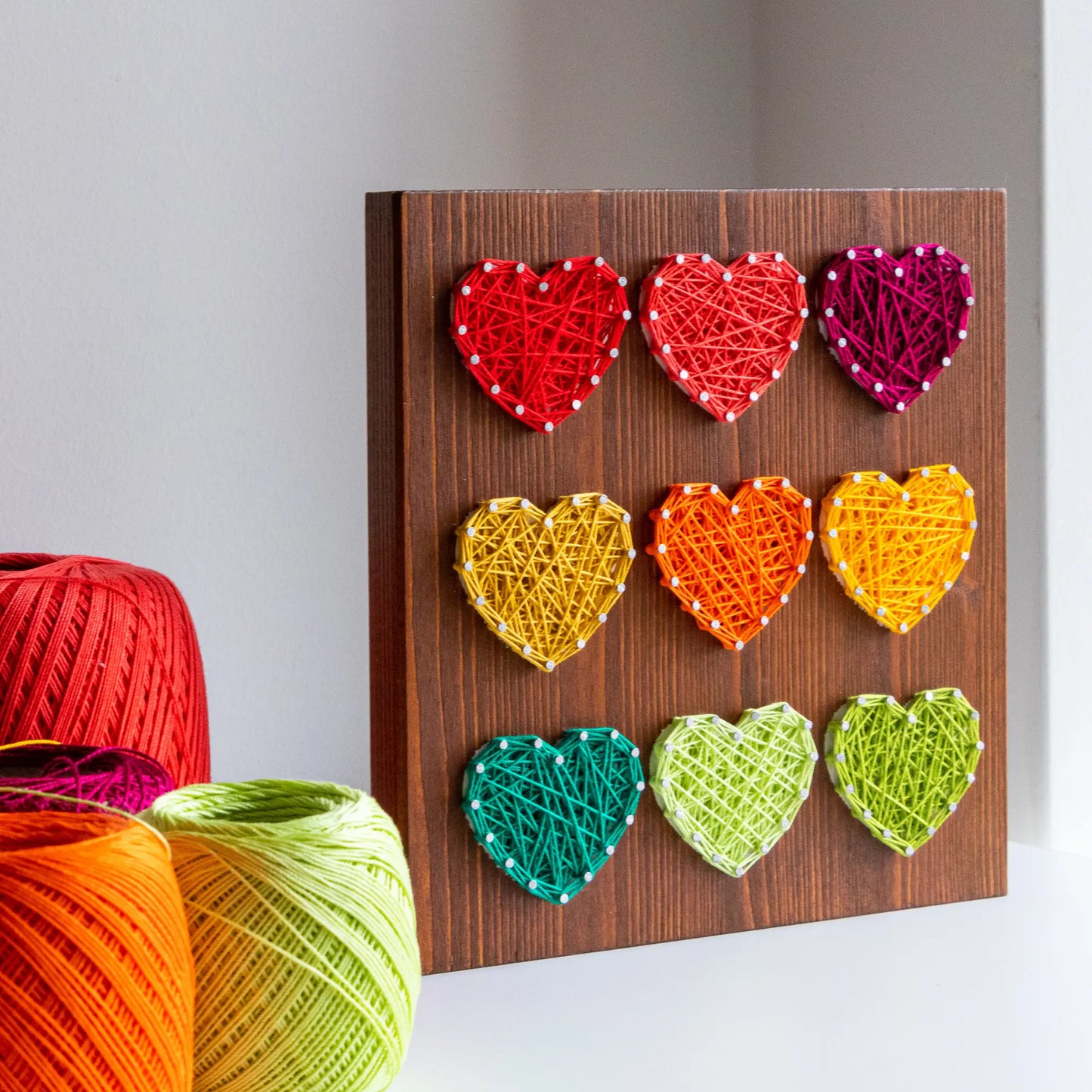 DIY string art kit with colorful hearts on a rustic wooden board by GoodStrings - view from side