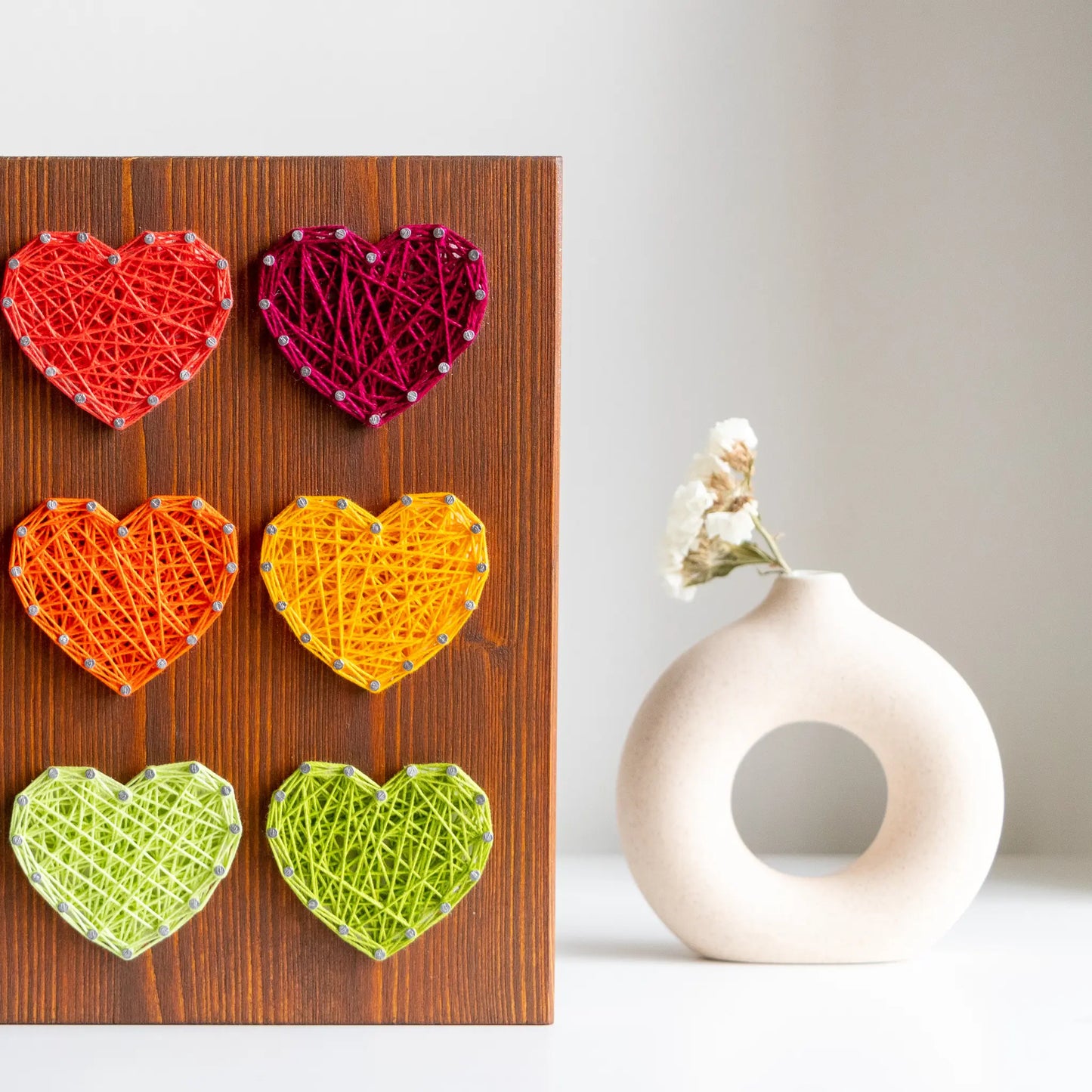 DIY string art kit with colorful hearts on a rustic wooden board by GoodStrings - partial. view from front, details