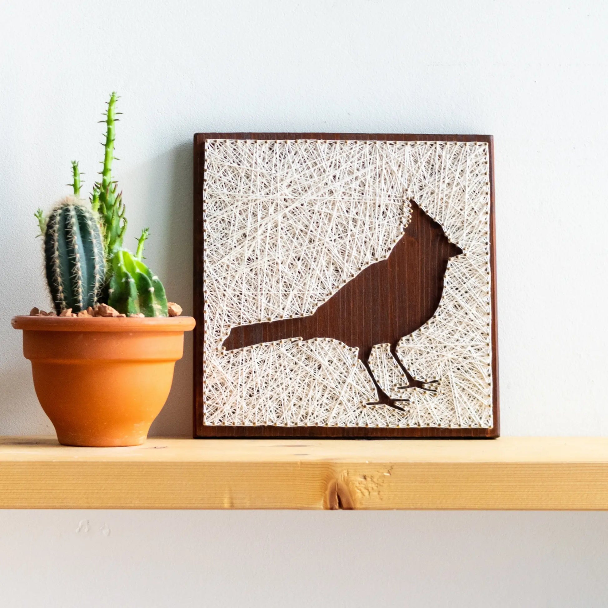 front view of a cardinal bird string art sign showing detailed string pattern on a dark wooden frame, resting on a wooden surface.