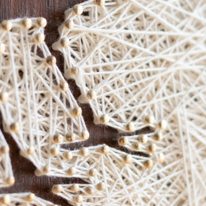 Side angle of a cardinal bird string art sign showing detailed string pattern on a dark wooden frame, resting on a wooden surface.