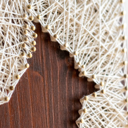 Side angle of a cardinal bird string art sign showing detailed string pattern on a dark wooden frame, resting on a wooden surface.