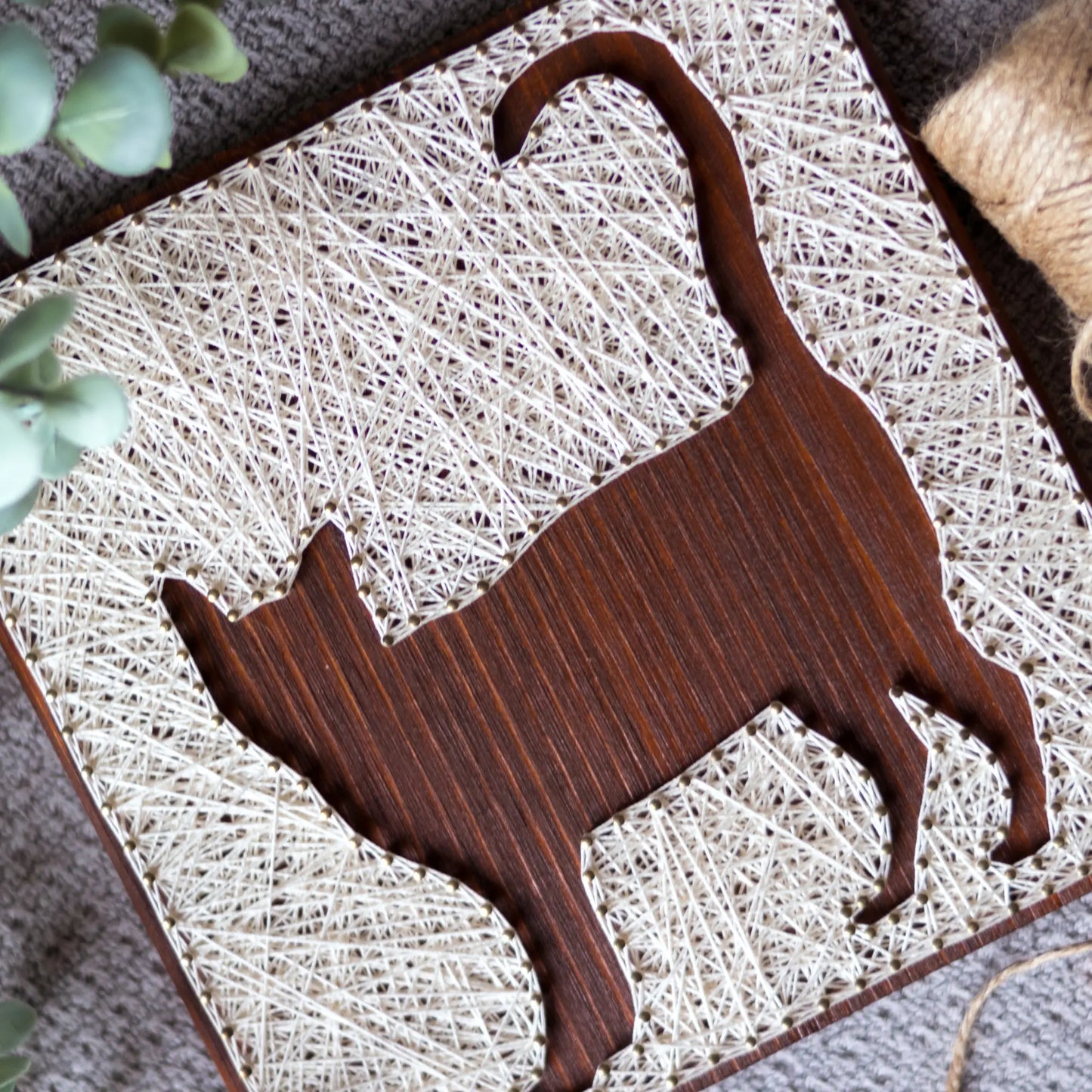 A close-up view of a DIY cat string art sign, featuring intricate white string patterns on a dark wooden background.