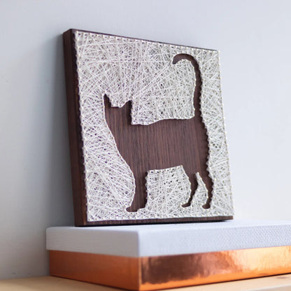 A close-up view of a DIY cat string art sign, featuring intricate white string patterns on a dark wooden background.