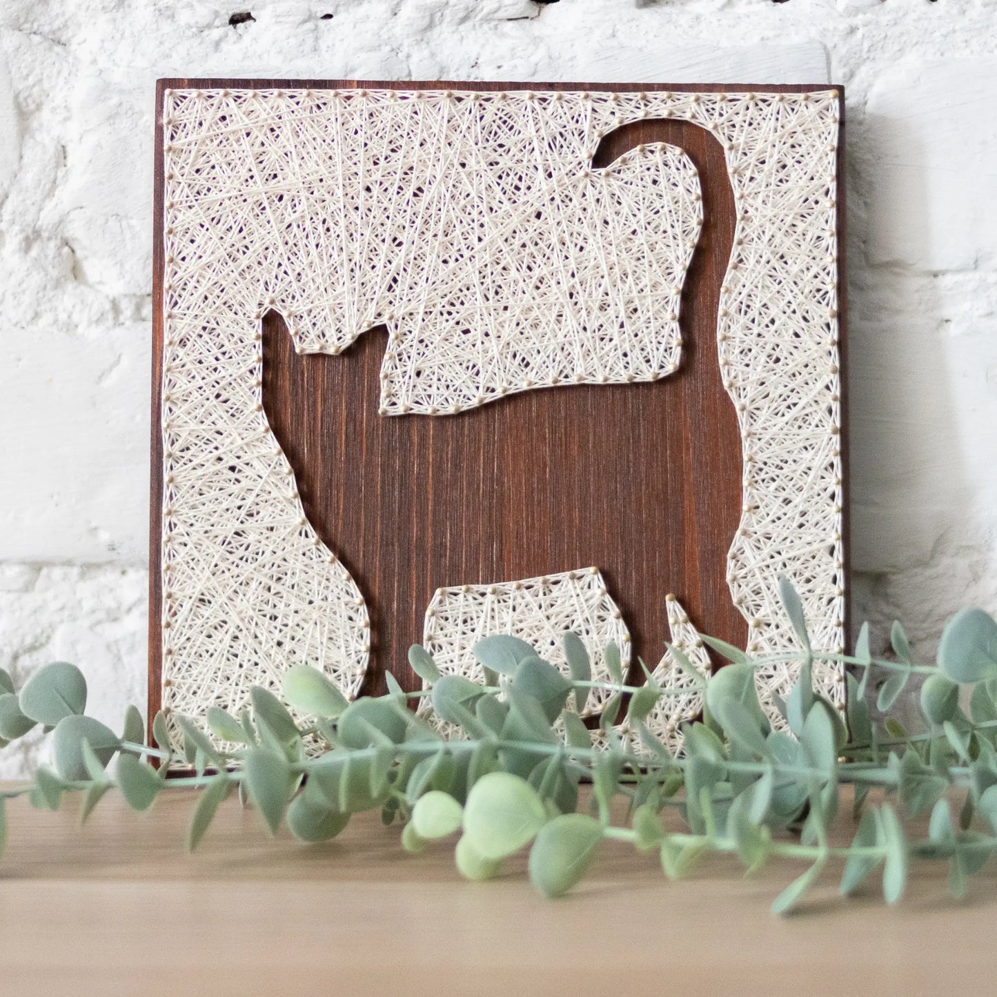 A close-up view of a DIY cat string art sign, featuring intricate white string patterns on a dark wooden background.