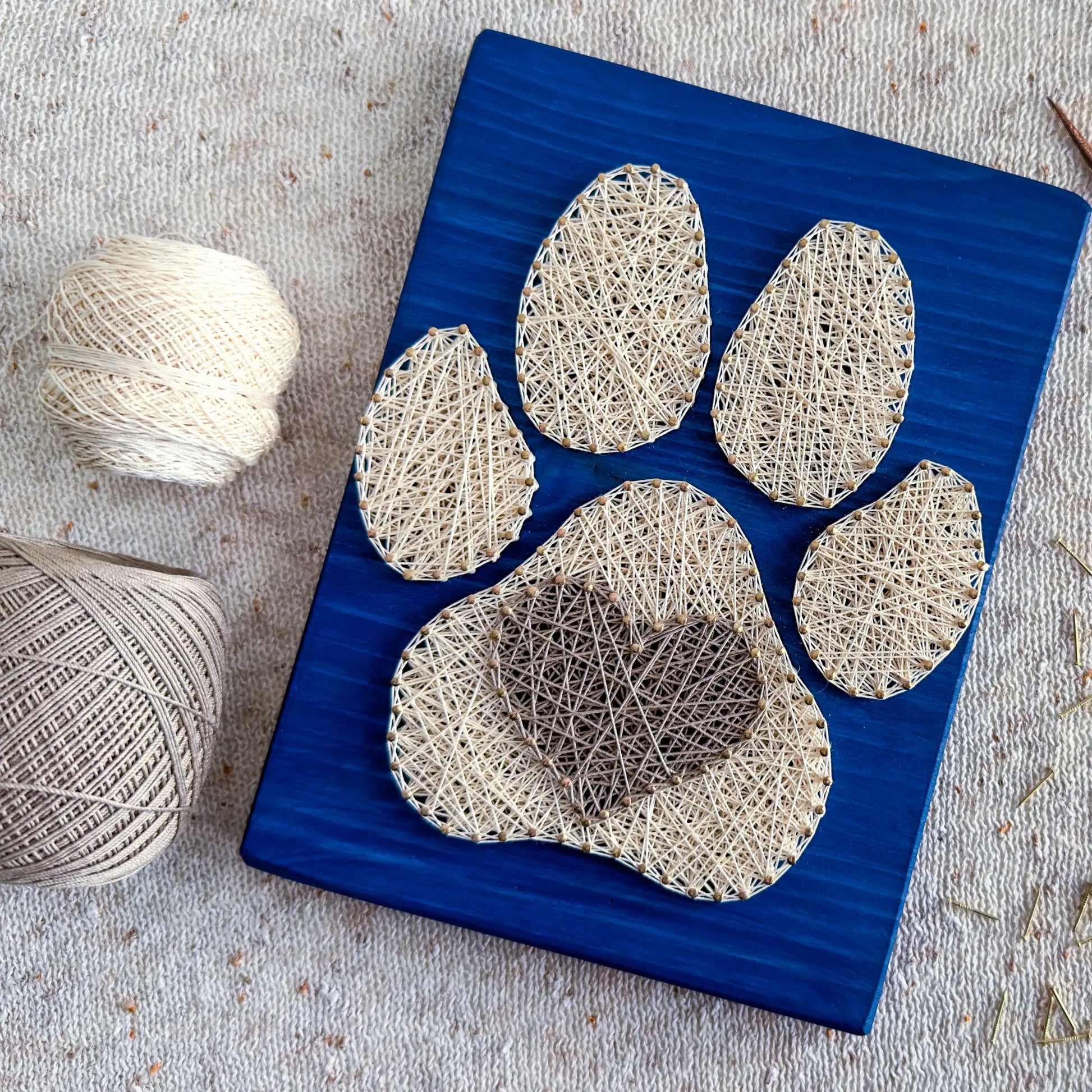  charming dog paw print string art sign made with white and dark brown string on a blue wooden background, featuring a heart shape in the center of the paw print.