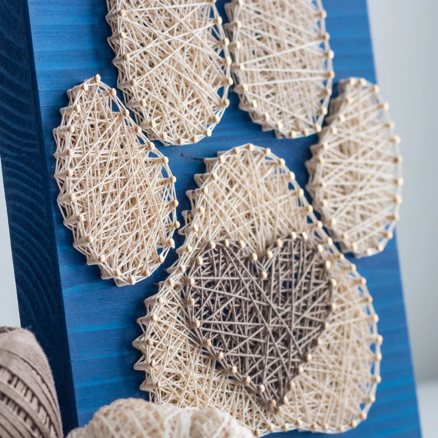  charming dog paw print string art sign made with white and dark brown string on a blue wooden background, featuring a heart shape in the center of the paw print.