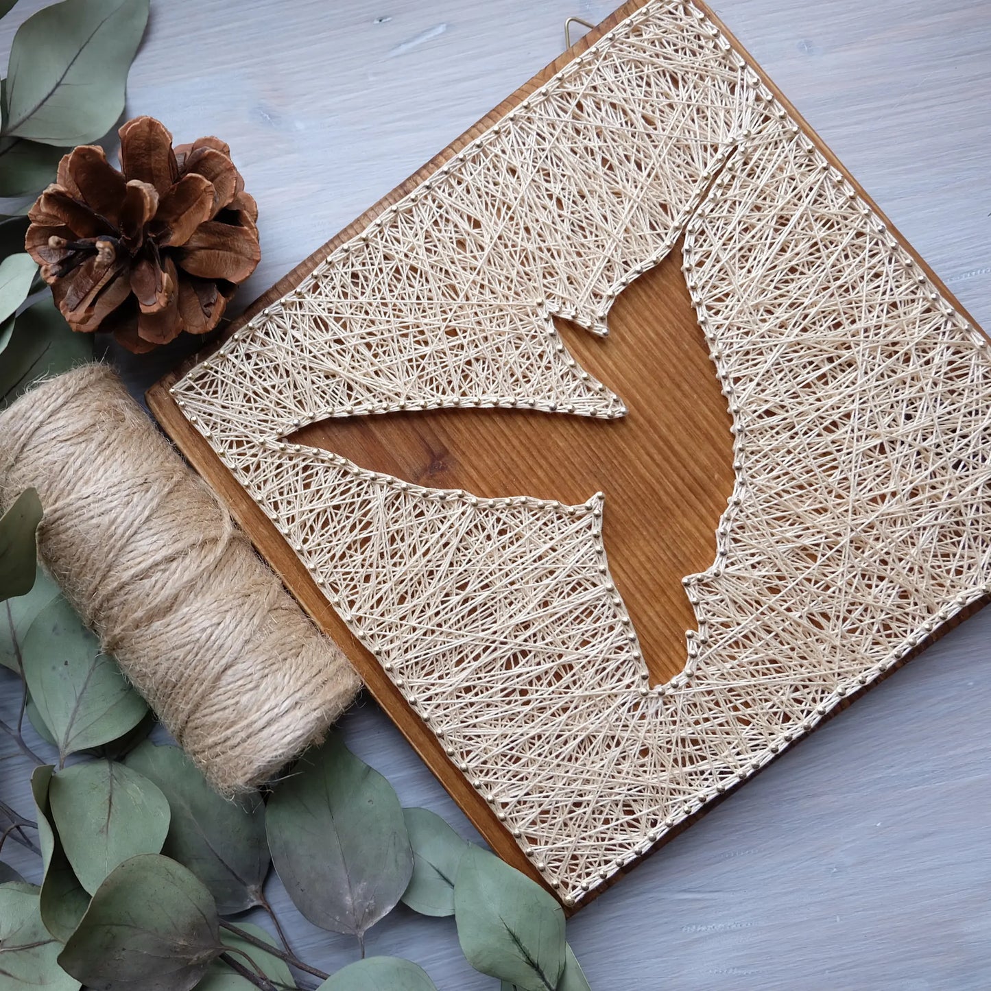 A beautiful hummingbird string art sign made with white string on a dark wooden background, depicting a hummingbird in mid-flight.