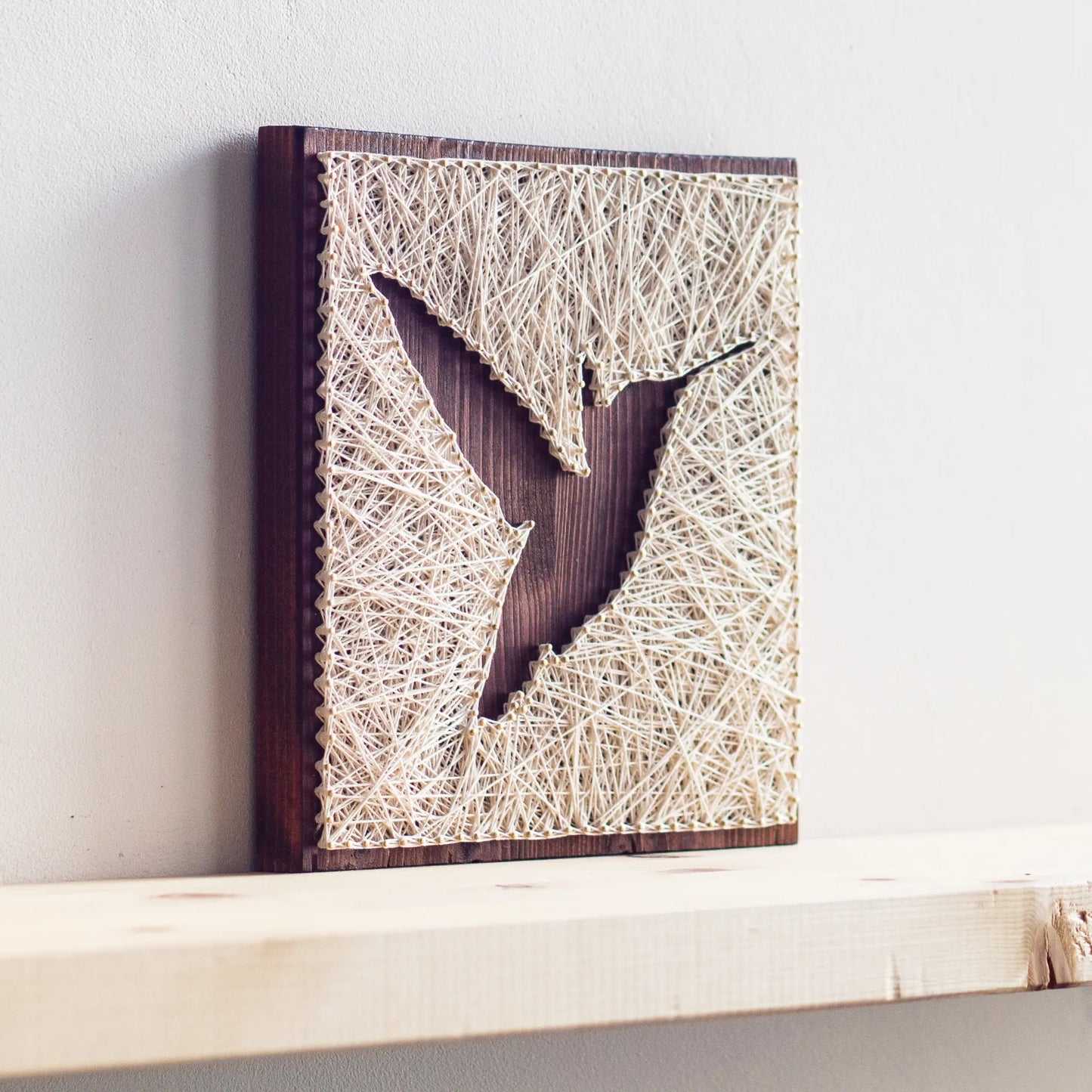 A beautiful hummingbird string art sign made with white string on a dark wooden background, depicting a hummingbird in mid-flight.