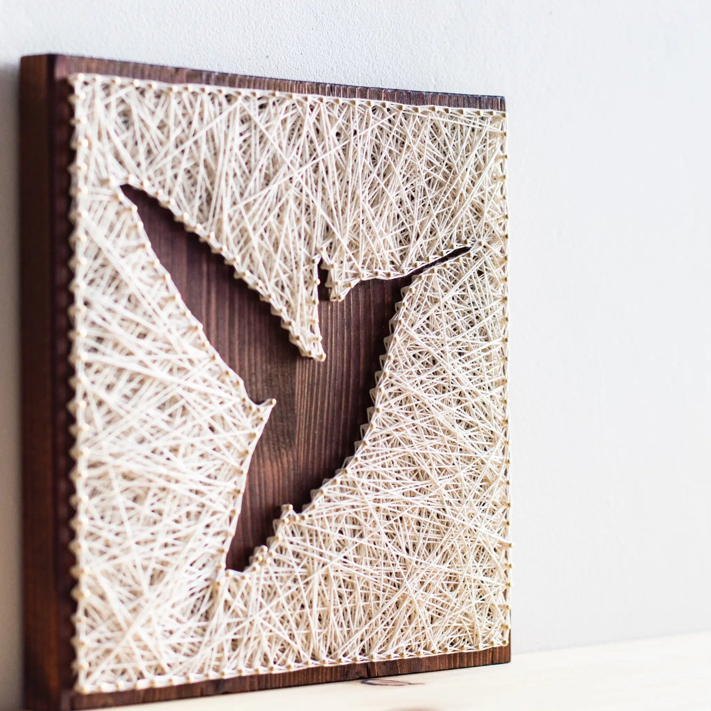 A beautiful hummingbird string art sign made with white string on a dark wooden background, depicting a hummingbird in mid-flight.