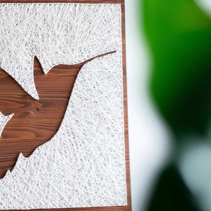 A beautiful hummingbird string art sign made with white string on a dark wooden background, depicting a hummingbird in mid-flight.