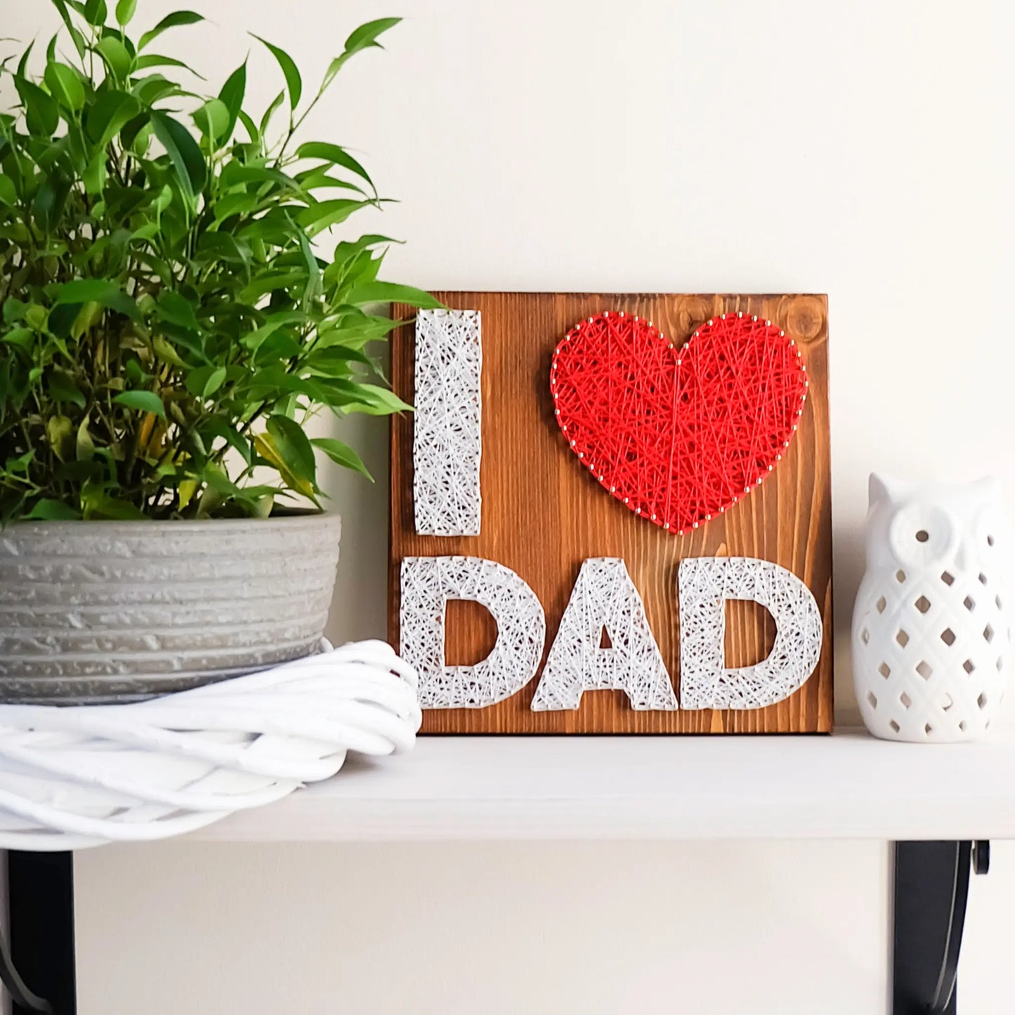 A heartfelt "I Love Dad" string art sign made with white and red string on a dark wooden background, featuring the words "I ♥ Dad" with a red heart.