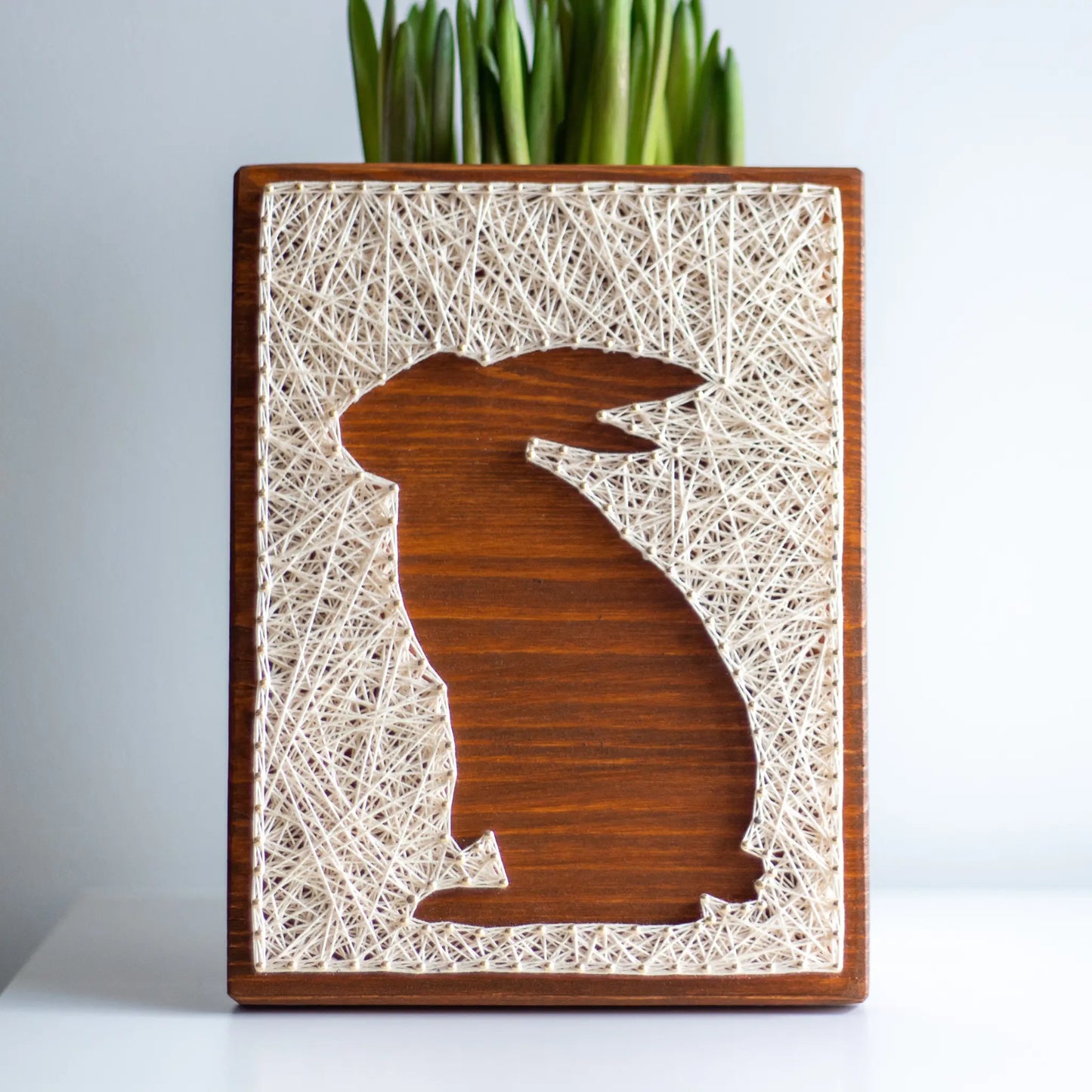 A charming rabbit string art sign made with white string on a dark wooden background, depicting a sitting rabbit silhouette.